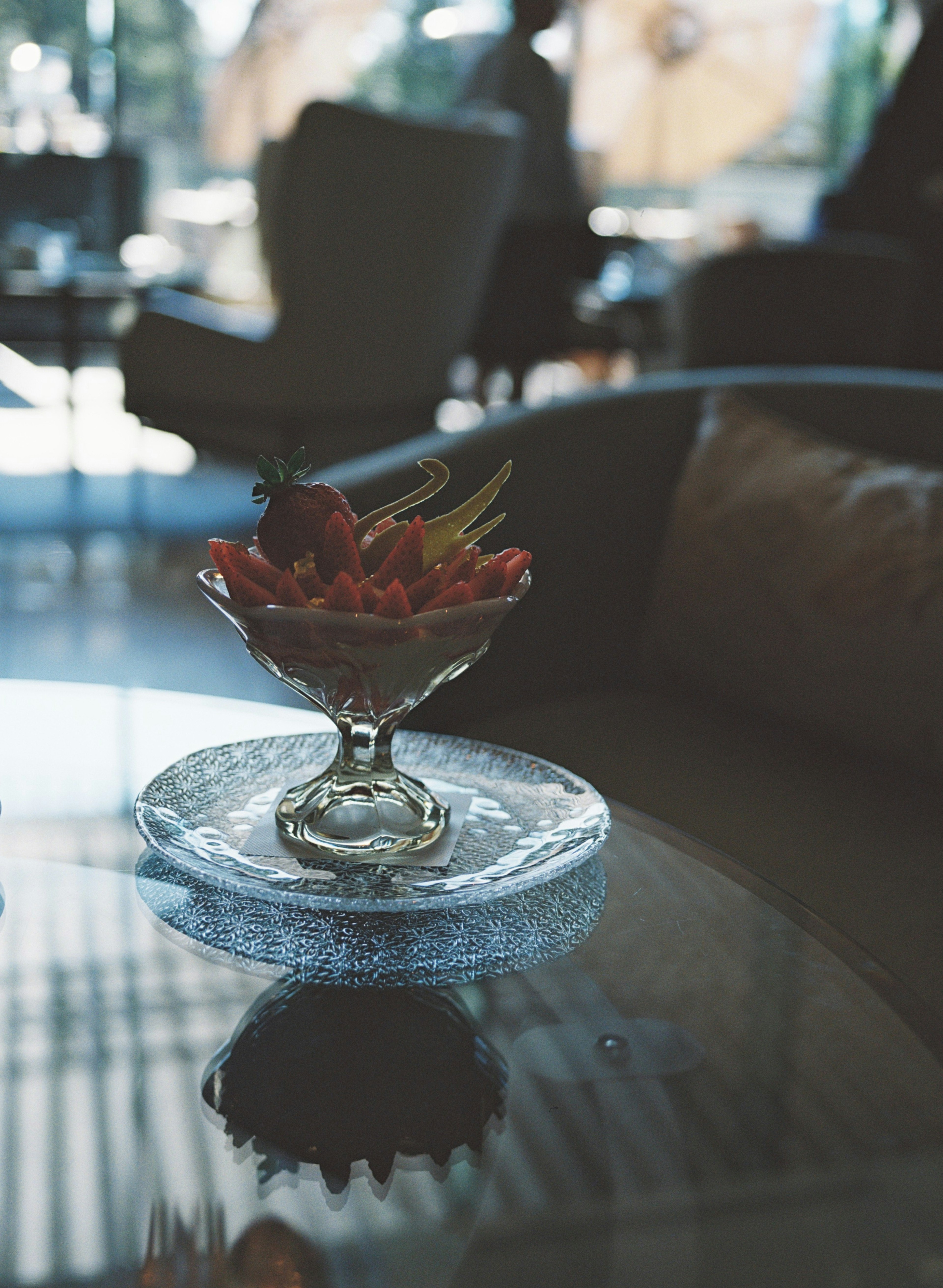 A glass bowl filled with fruit on a table with soft furnishings in the background