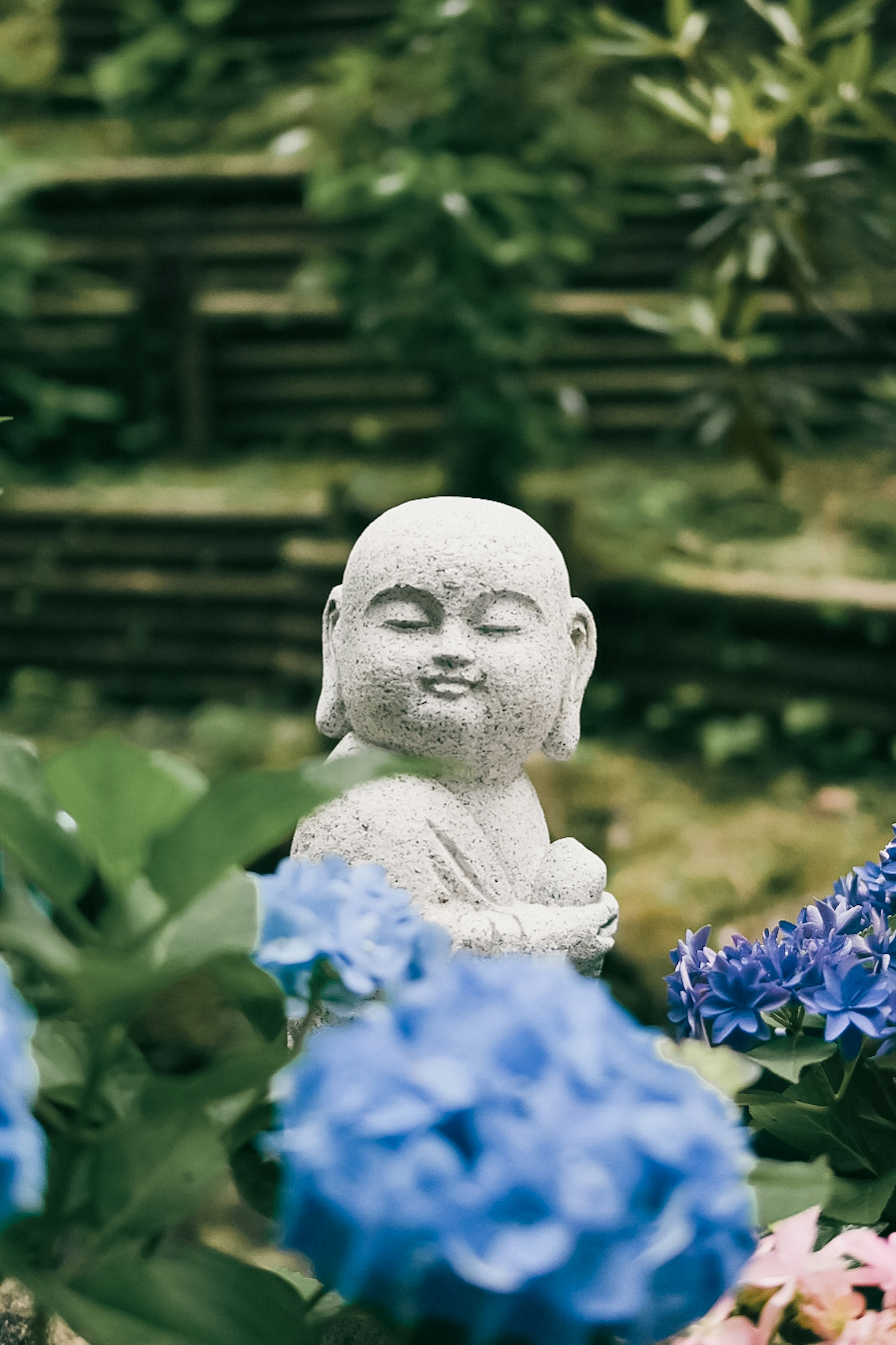 Steinstatue eines lächelnden Buddhas zwischen blauen Blumen