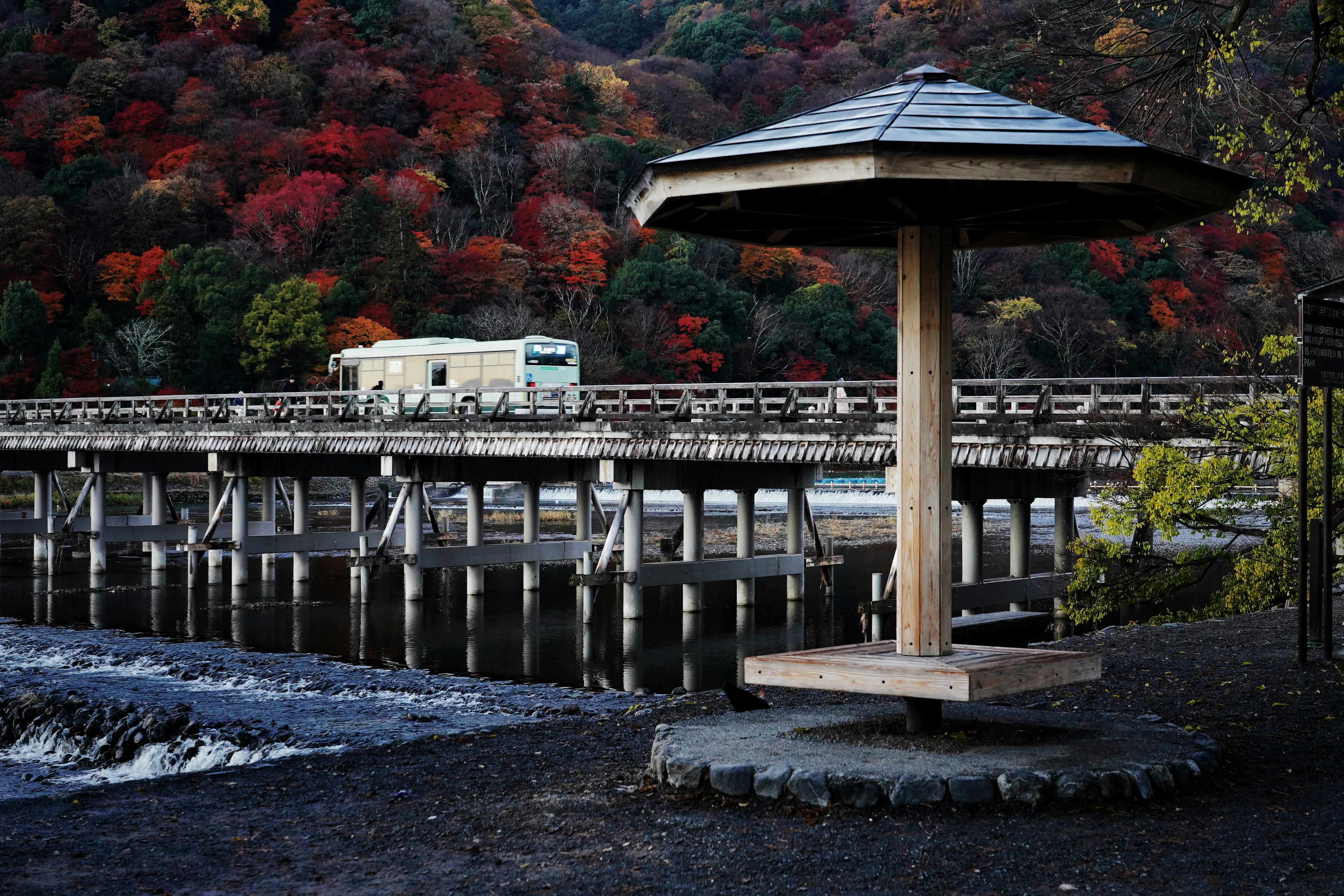 Wooden pavilion with autumn foliage backdrop and bridge