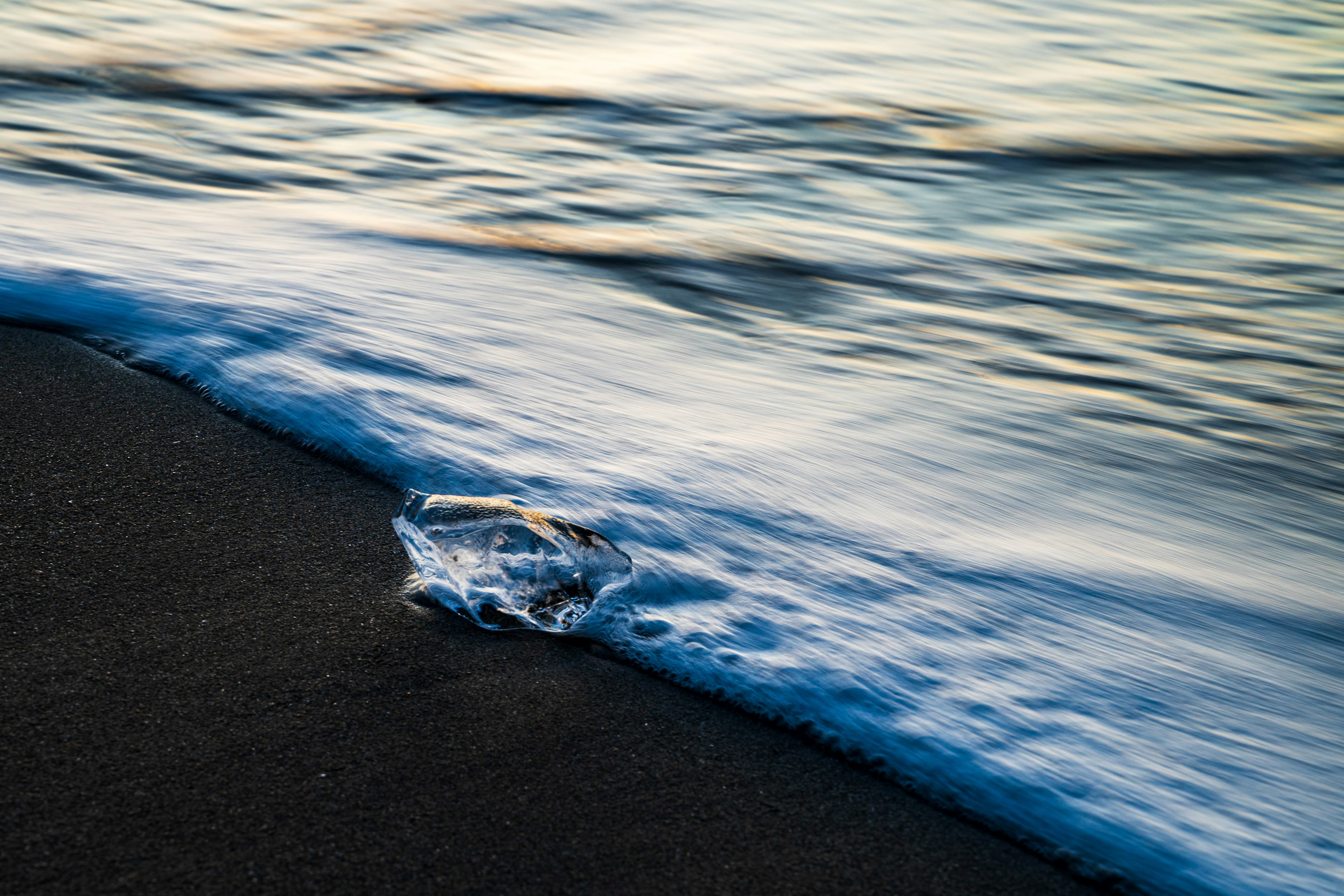 Imagen de un fragmento de hielo claro en una playa de arena con olas