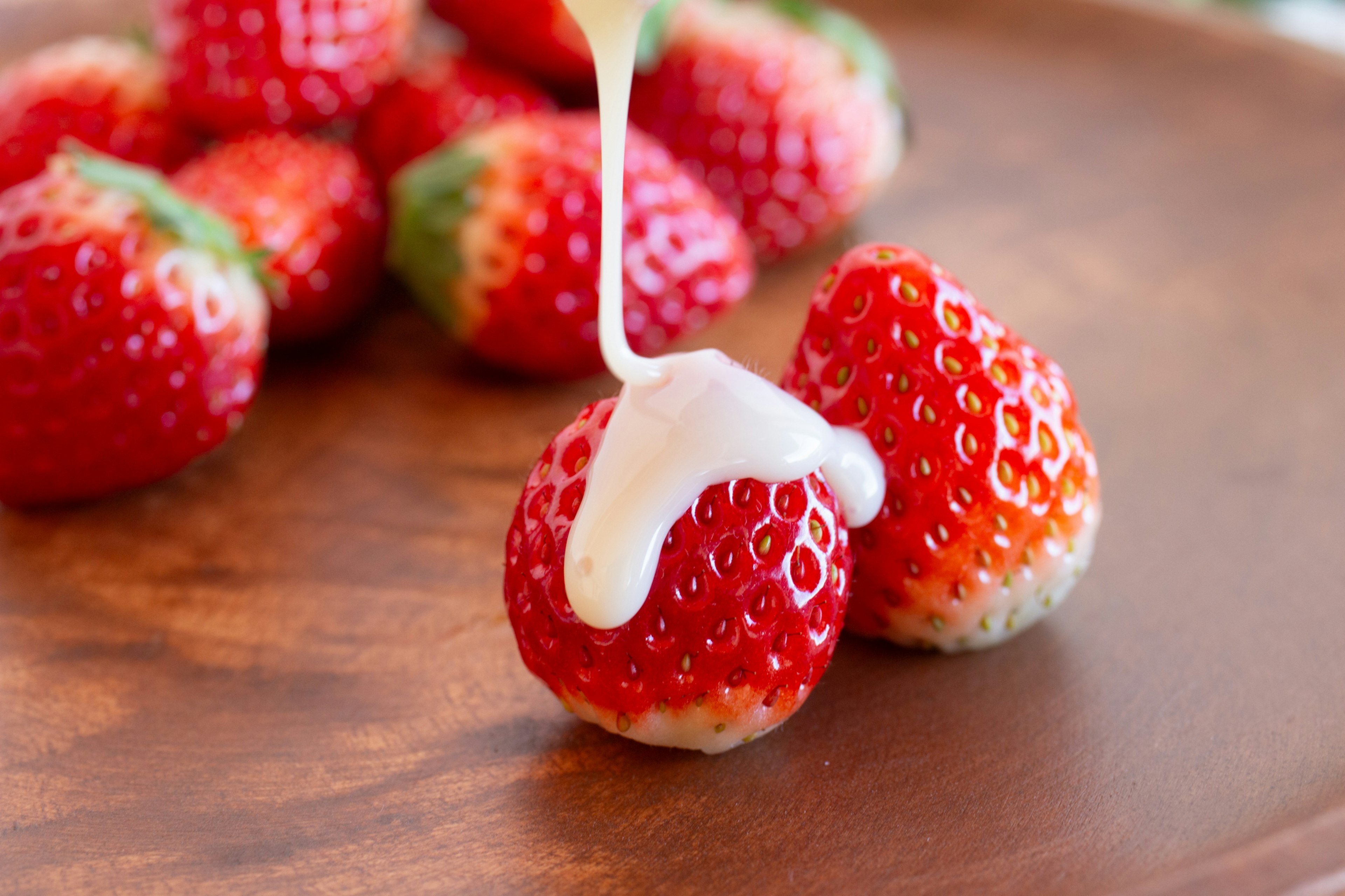 Fragole fresche guarnite con panna su un piatto di legno