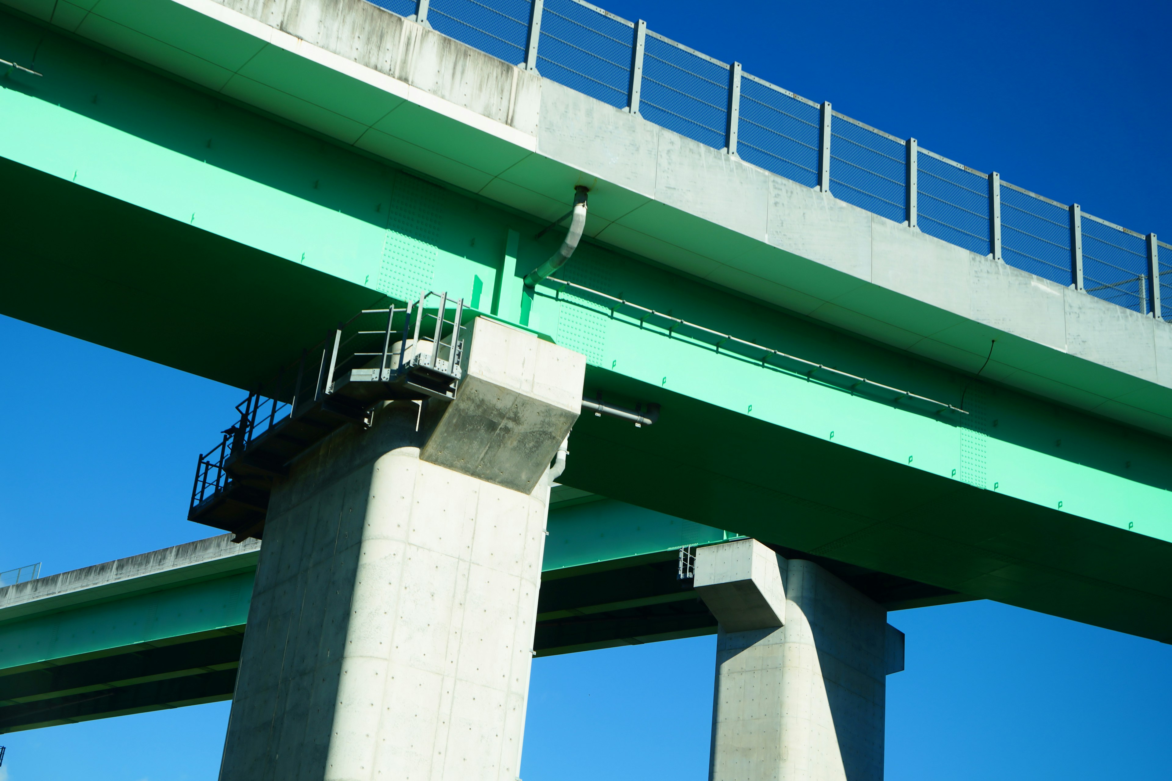 Tampilan detail struktur jembatan hijau di bawah langit biru