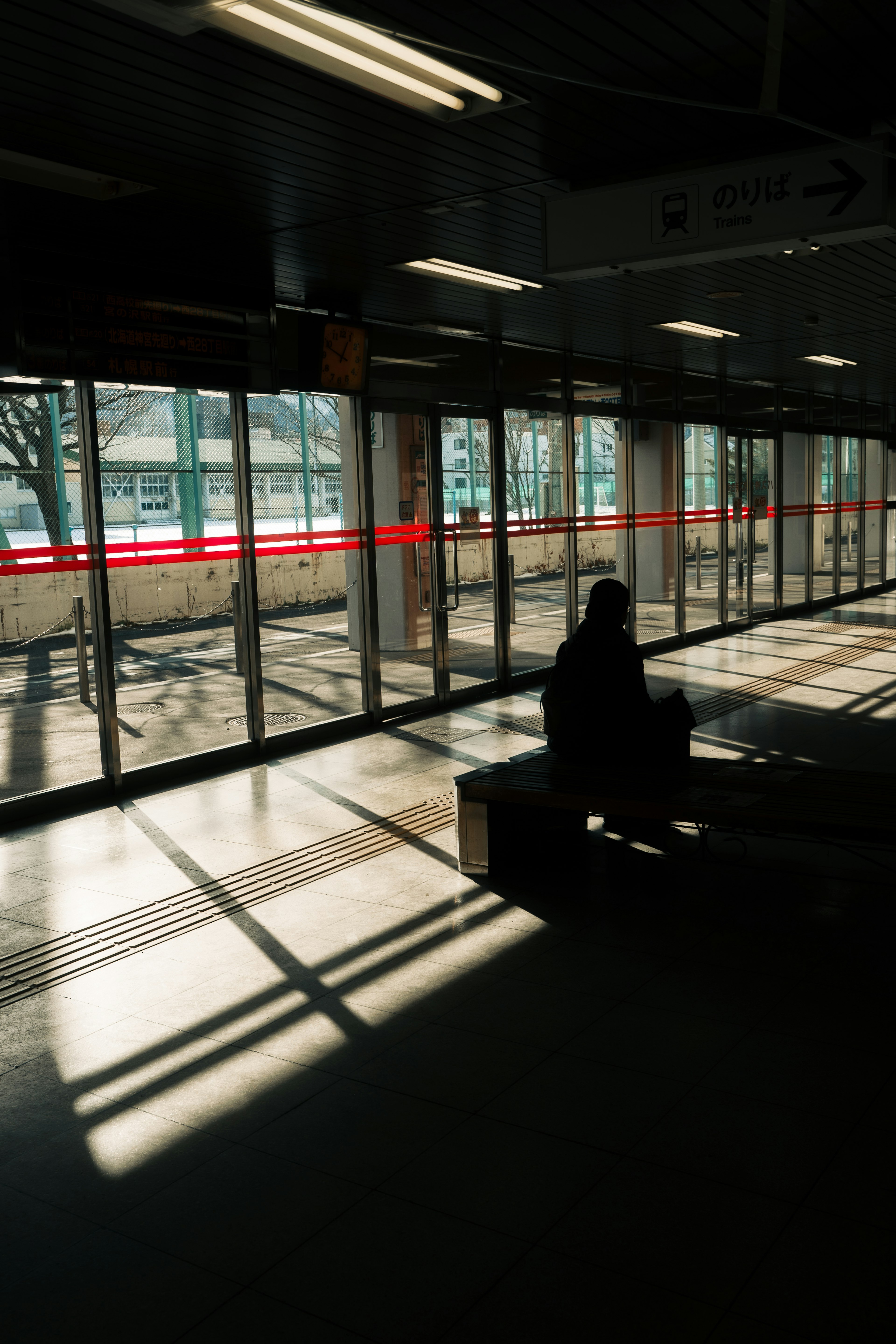 Silueta de una persona sentada en una sala de espera de estación con luz y sombras