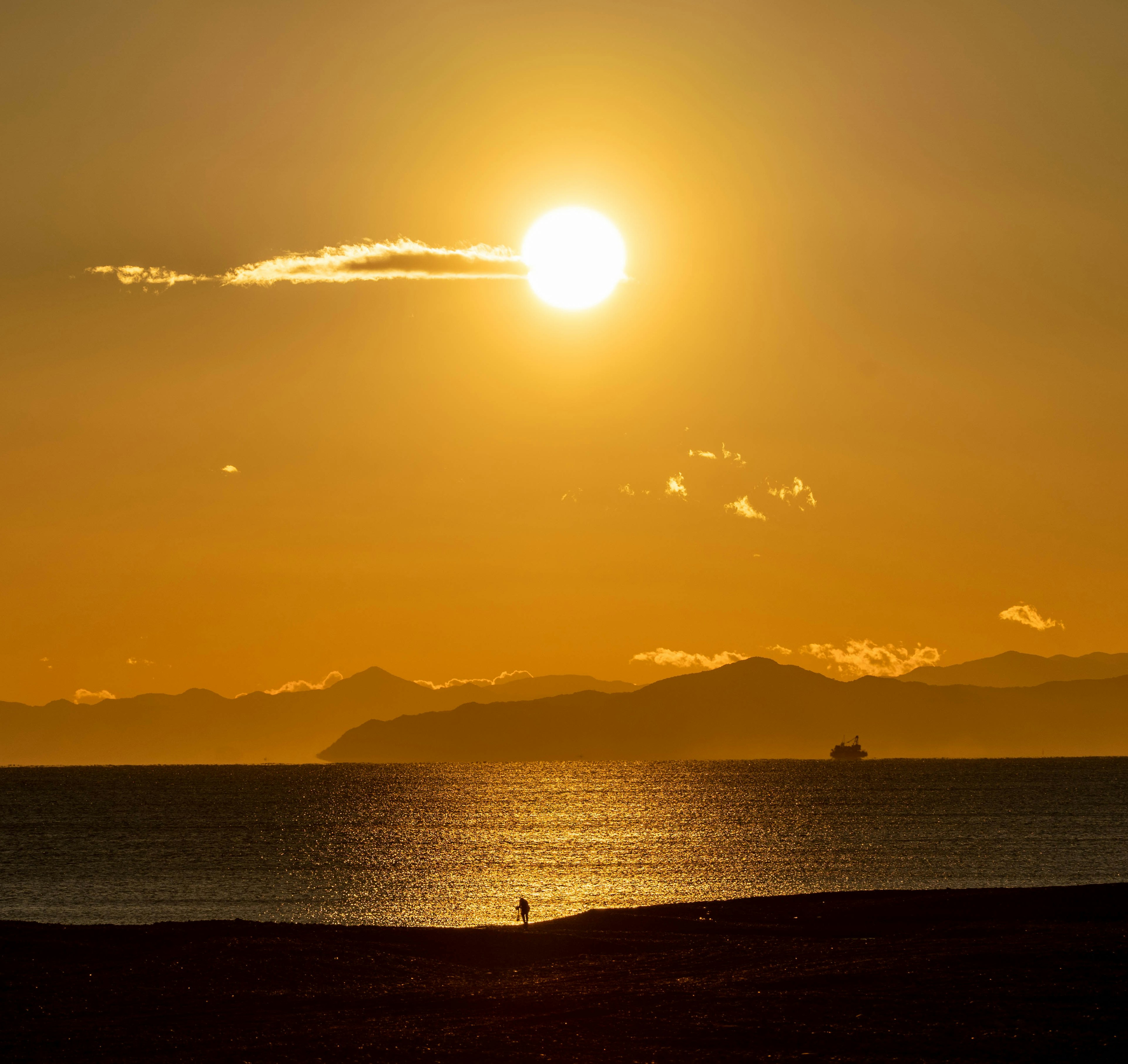 夕日が海に沈む美しい風景　遠くに山々と船