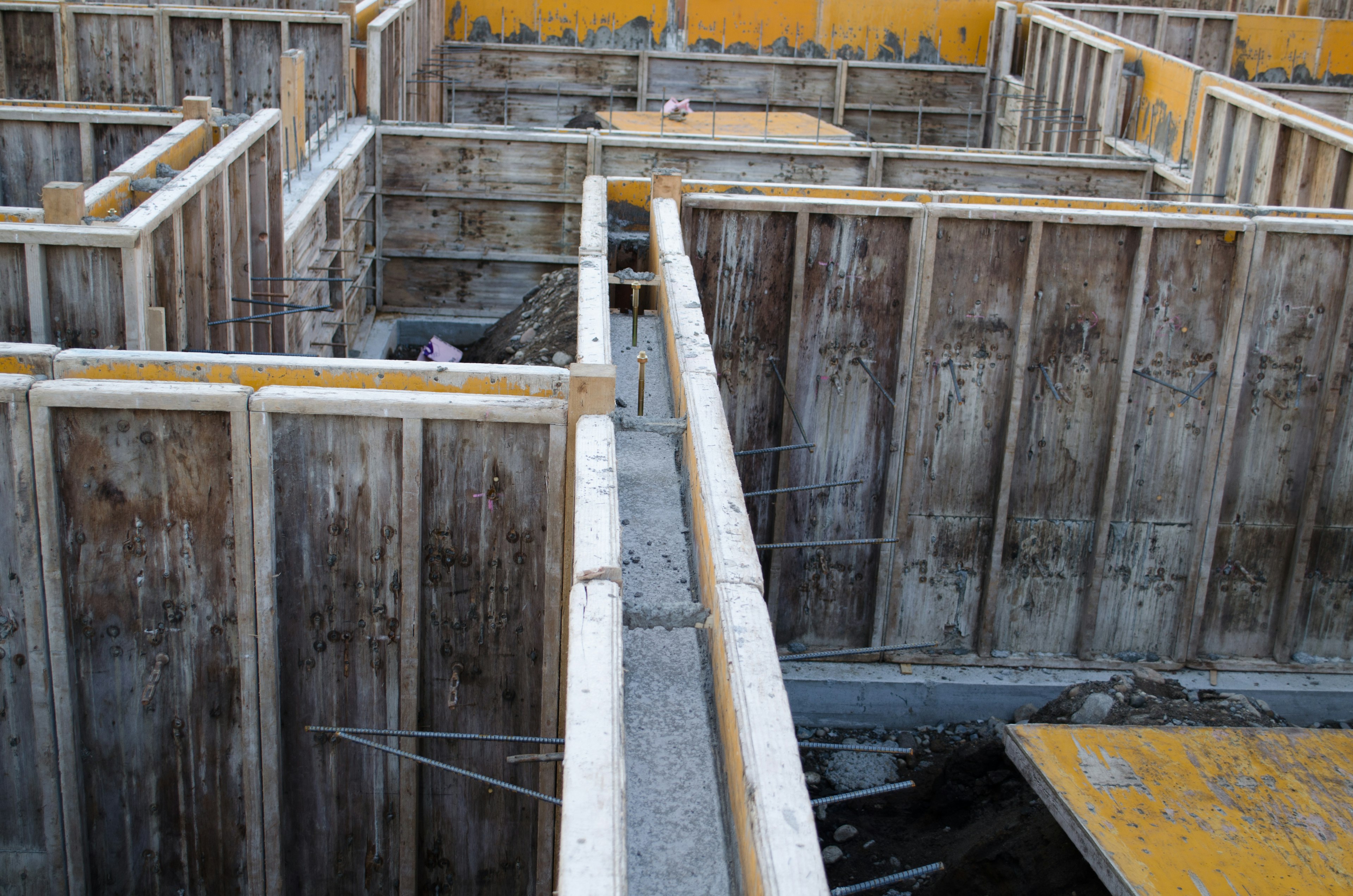 Chantier de construction montrant des travaux de fondation en béton avec des coffrages en bois et des supports en acier