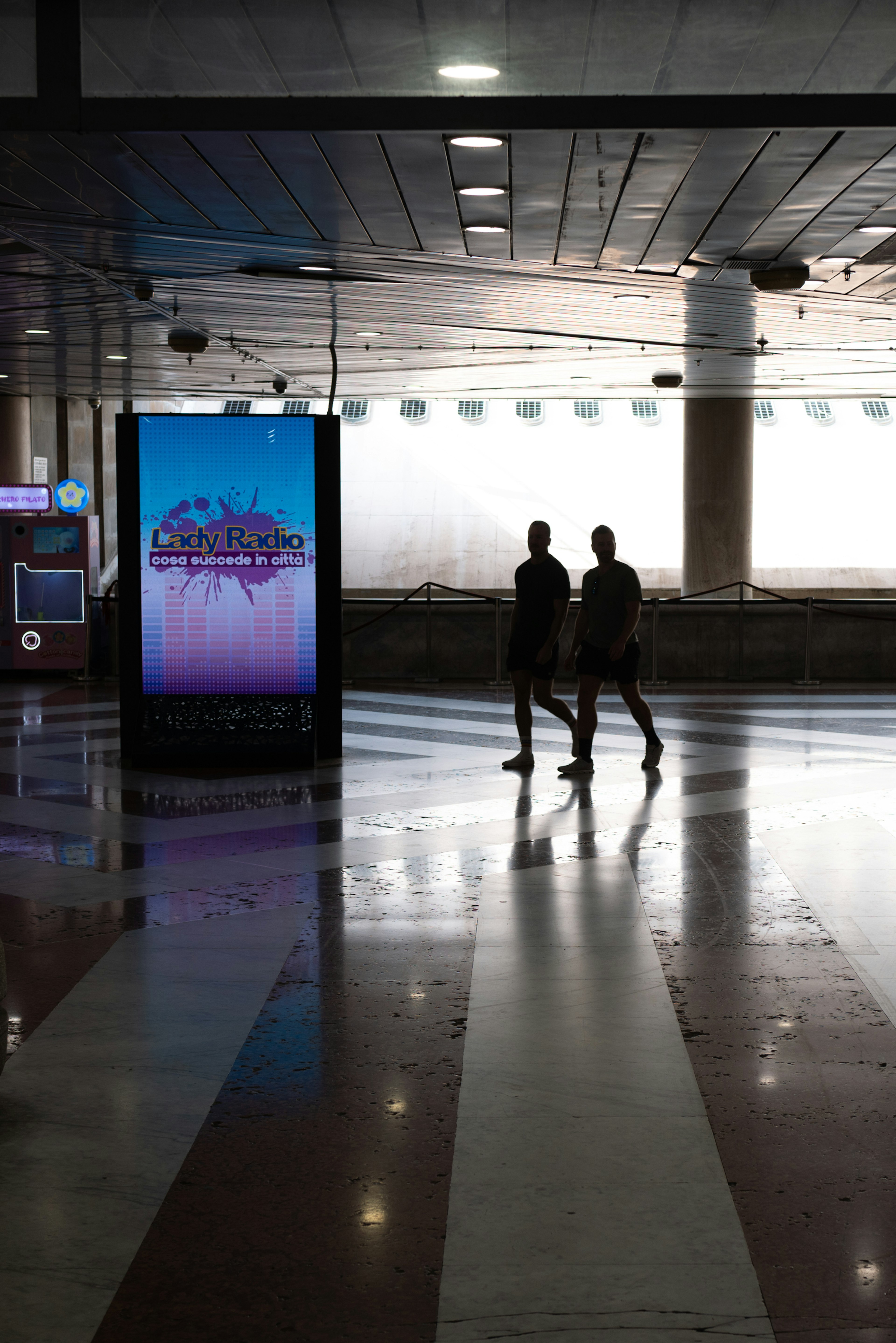 空港のロビーで歩く二人の人影と明るい広告