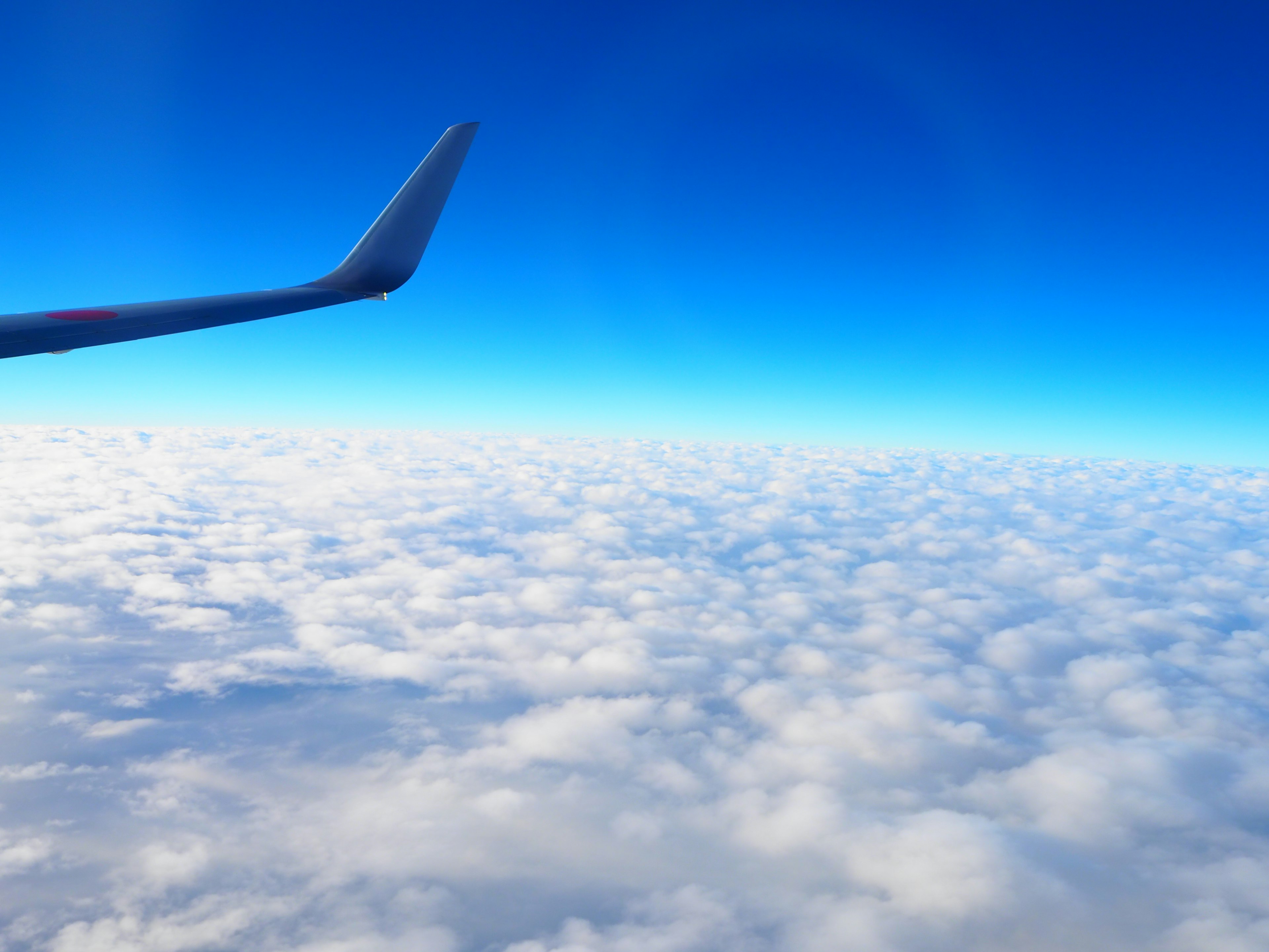 Clouds beneath a clear blue sky with an airplane wing