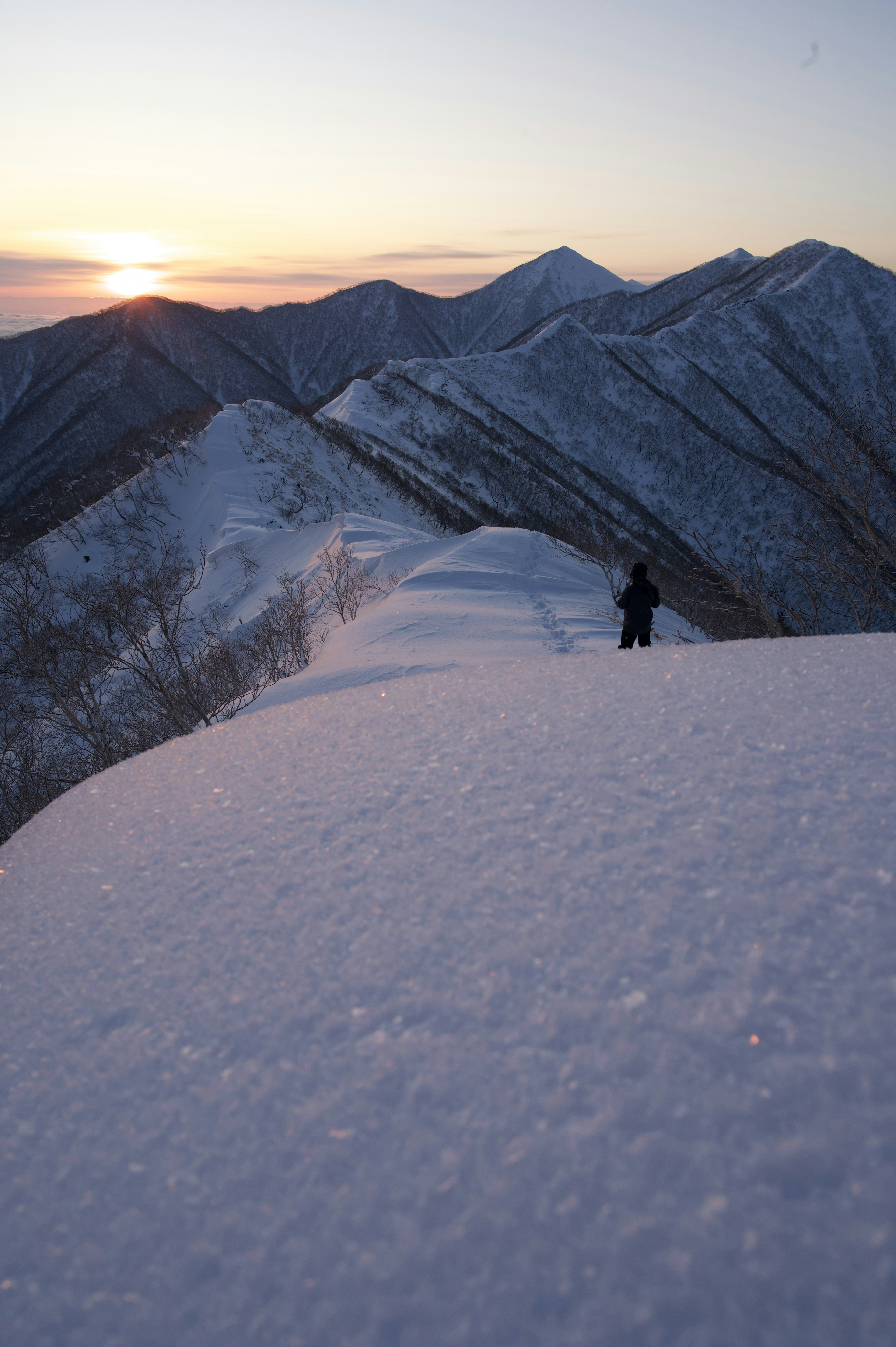 Silhouette di un escursionista su una cresta di montagna innevata con un tramonto sullo sfondo