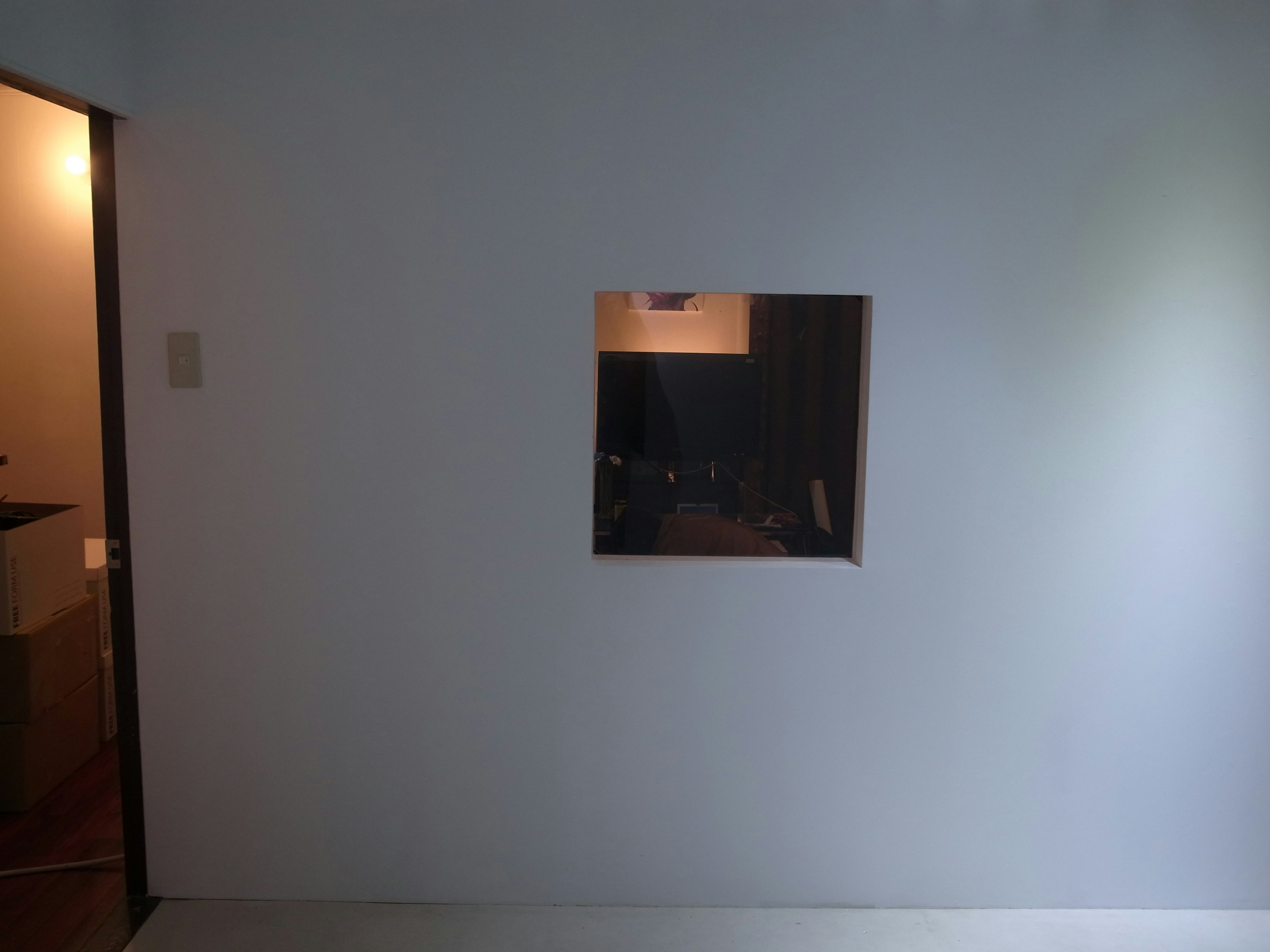 A small square window in a white wall revealing a dark room