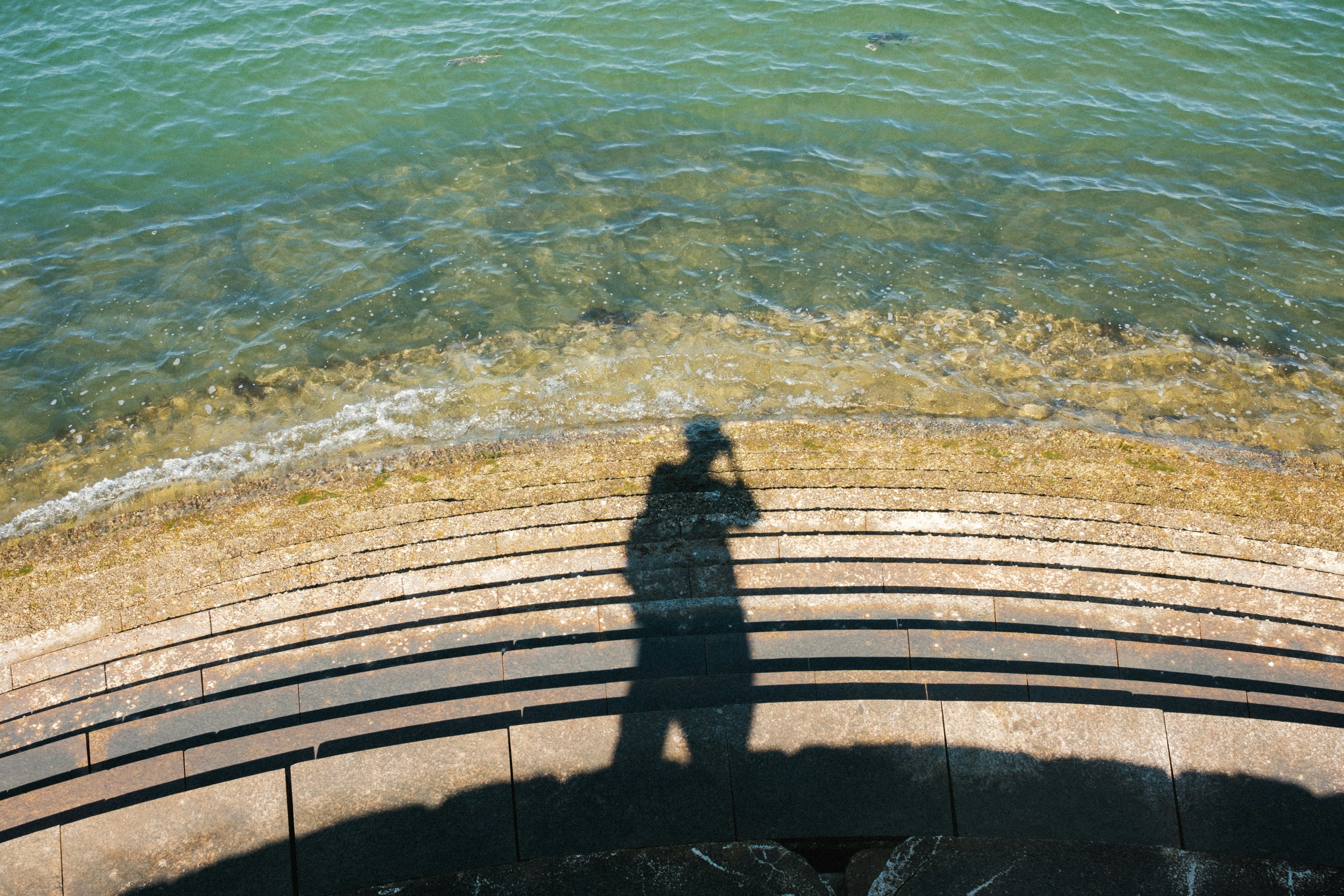 Ombre d'une personne sur des marches circulaires en pierre au bord de l'eau