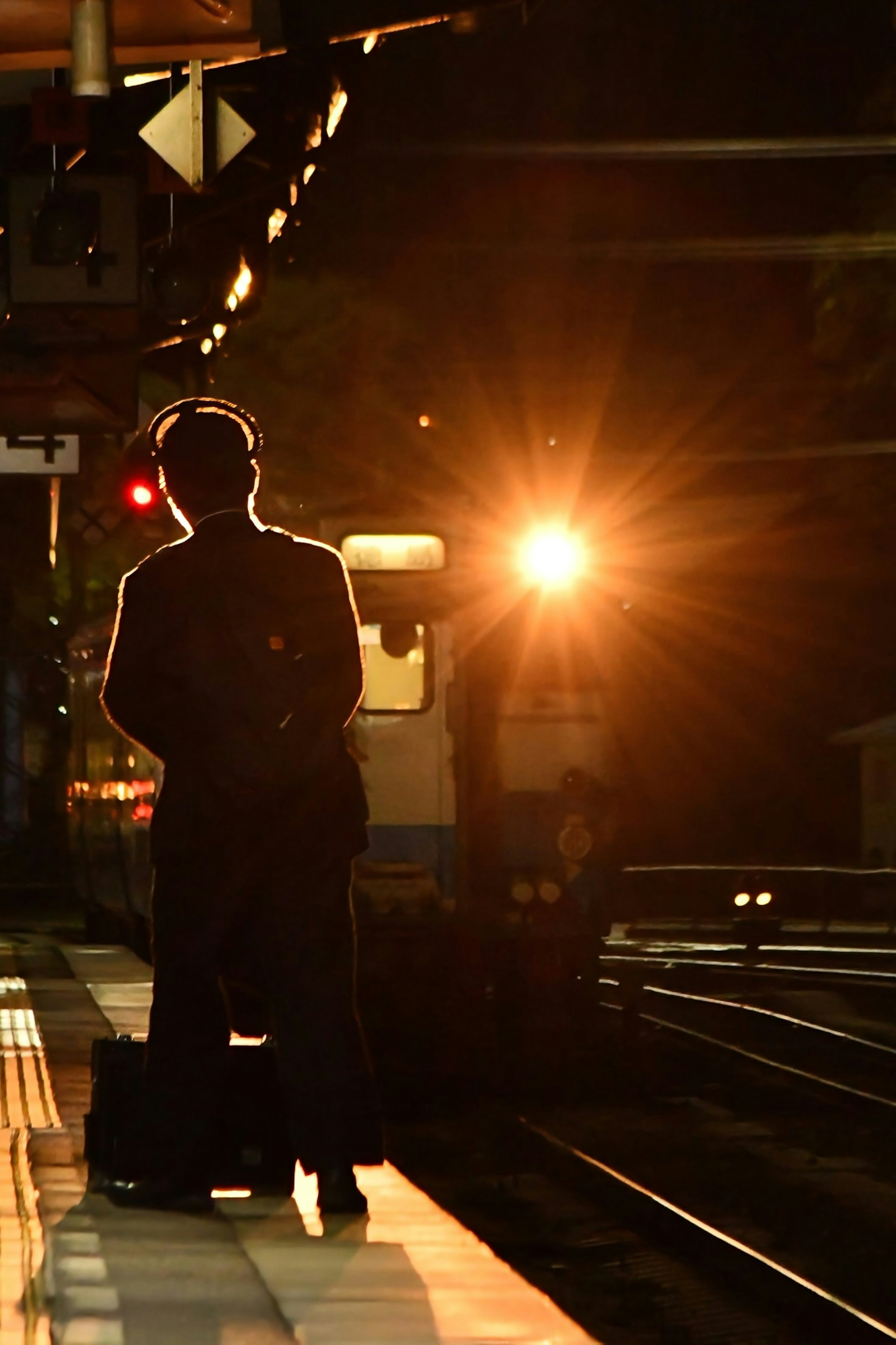 夜の駅で電車を待つ人影と明るい列車のライト