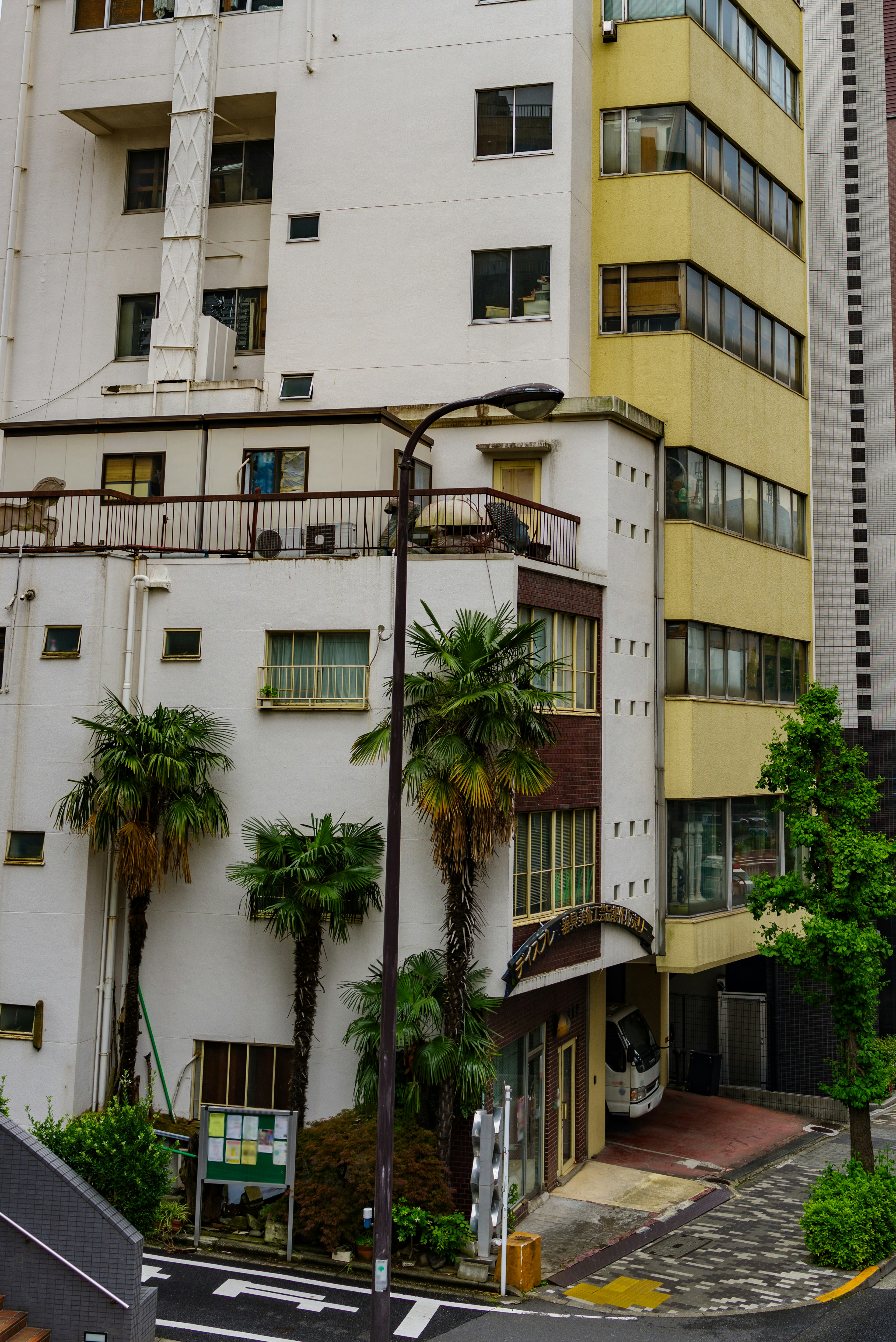 Street corner with a white and yellow building featuring palm trees and paved road