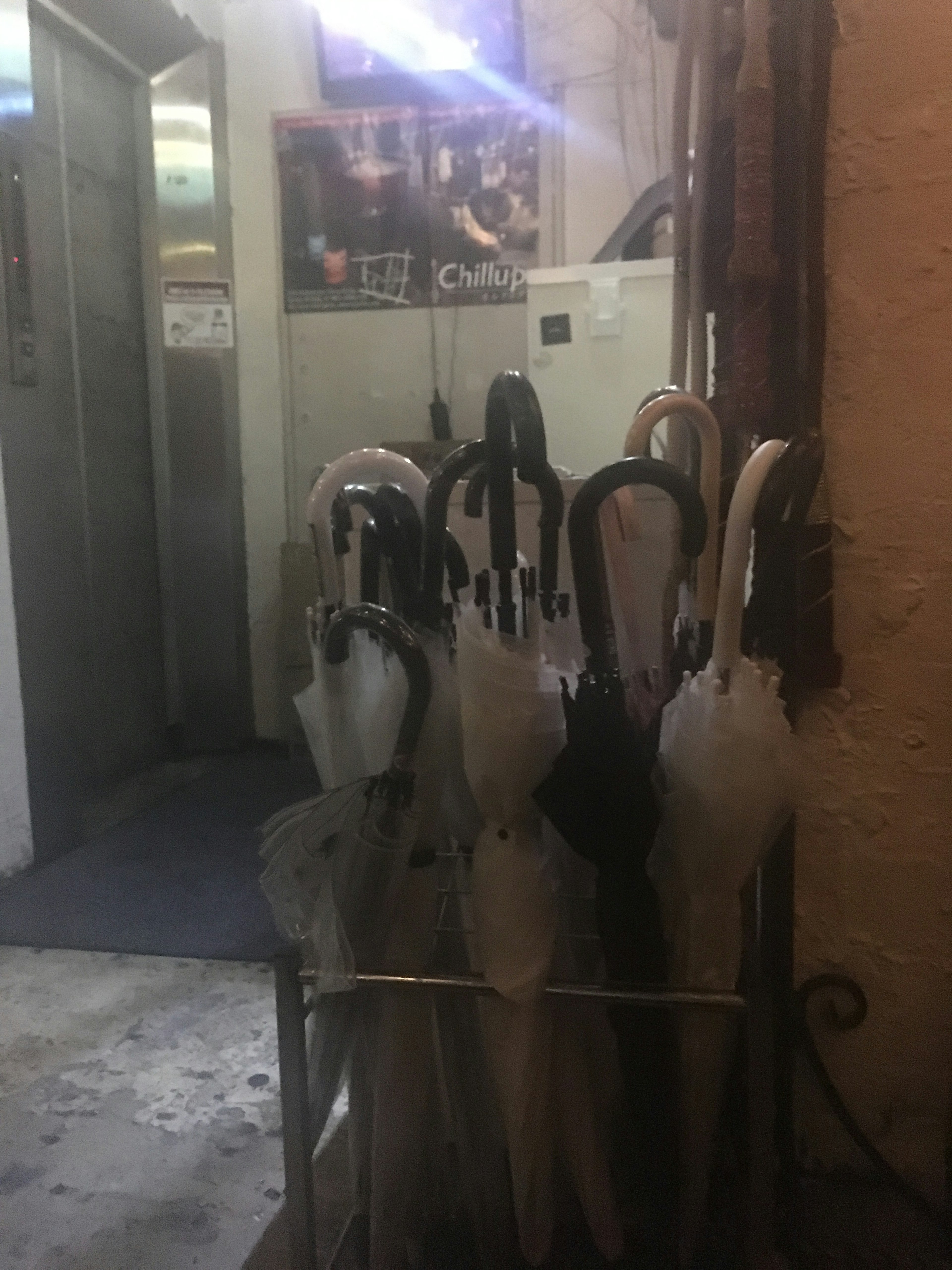 A collection of black and white umbrellas in a stand with an elevator and posters in the background