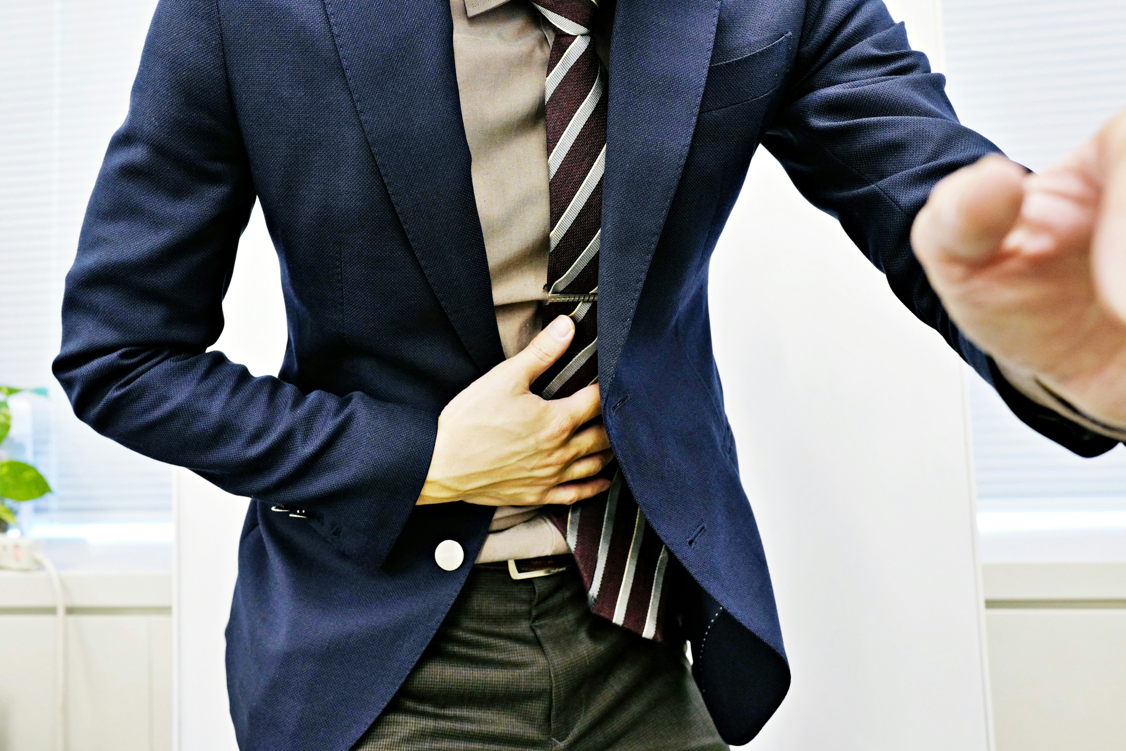 A man in a business suit holding his stomach with one hand while extending the other hand forward