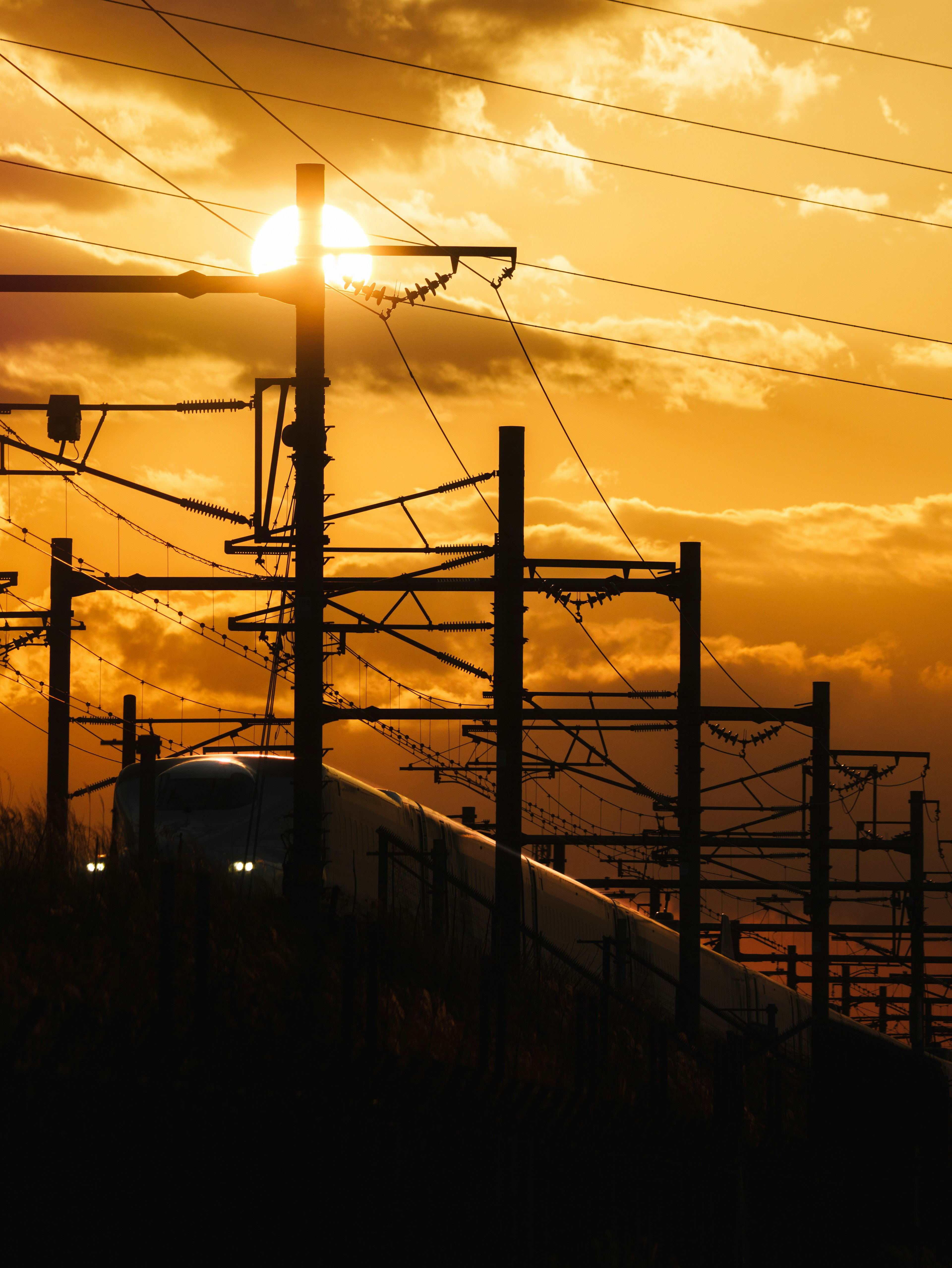 Silhouette d'un train et de poteaux électriques au coucher du soleil