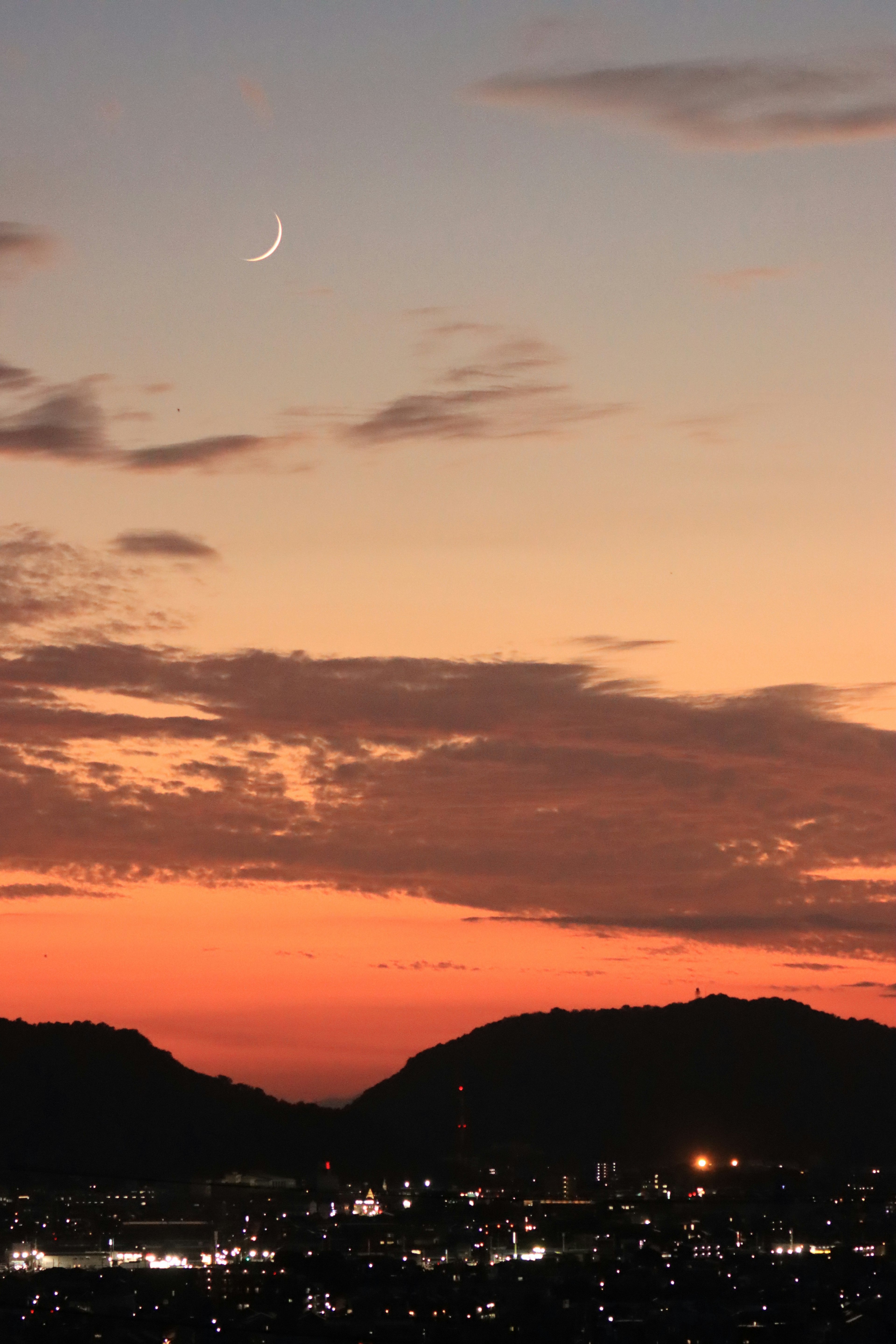 Silhouettierte Berge unter einem Sonnenuntergangshimmel mit einer schmalen Mondsichel