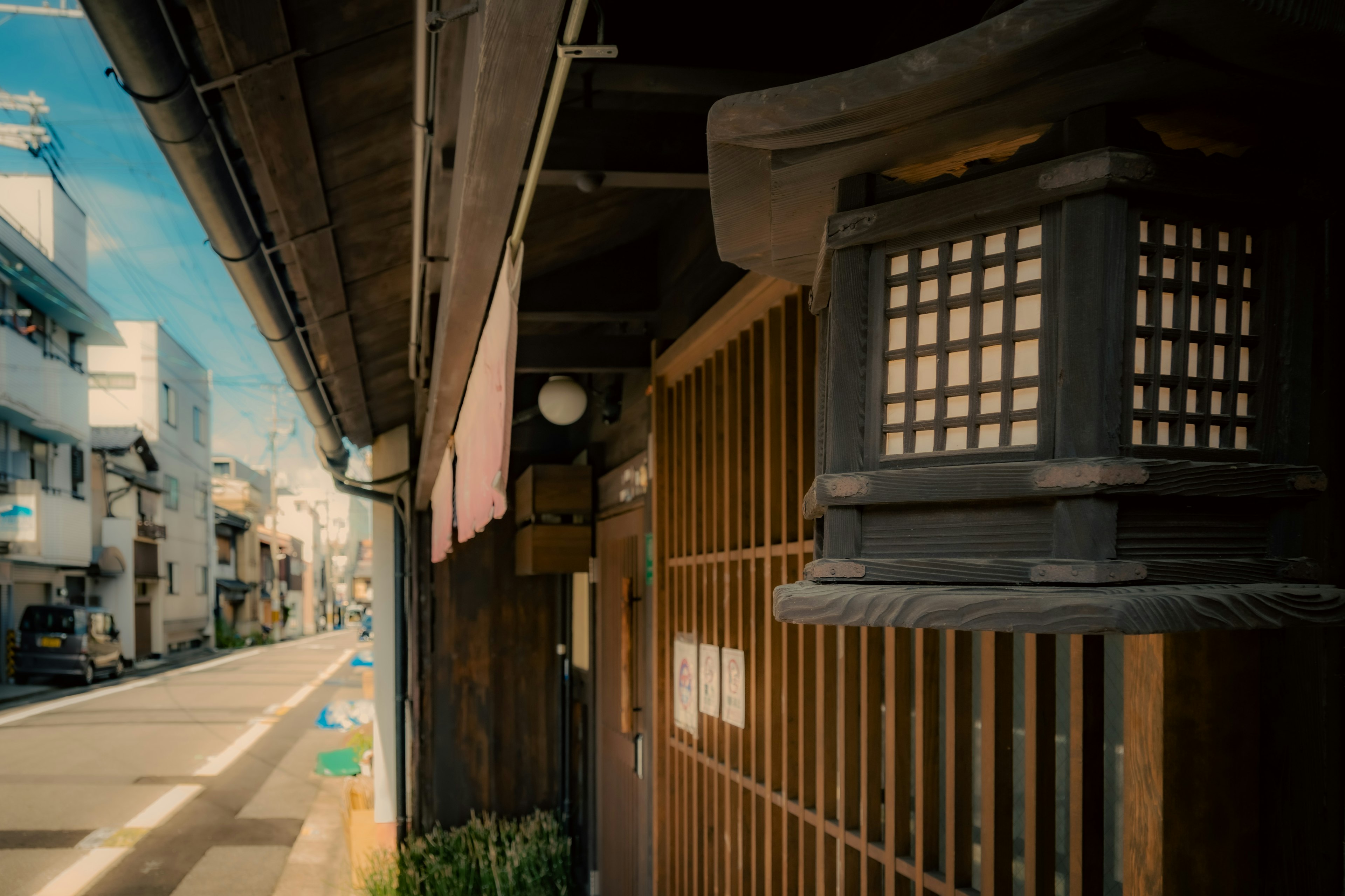 古い日本の街並みの一部である木製の格子窓とランタンが特徴的な風景