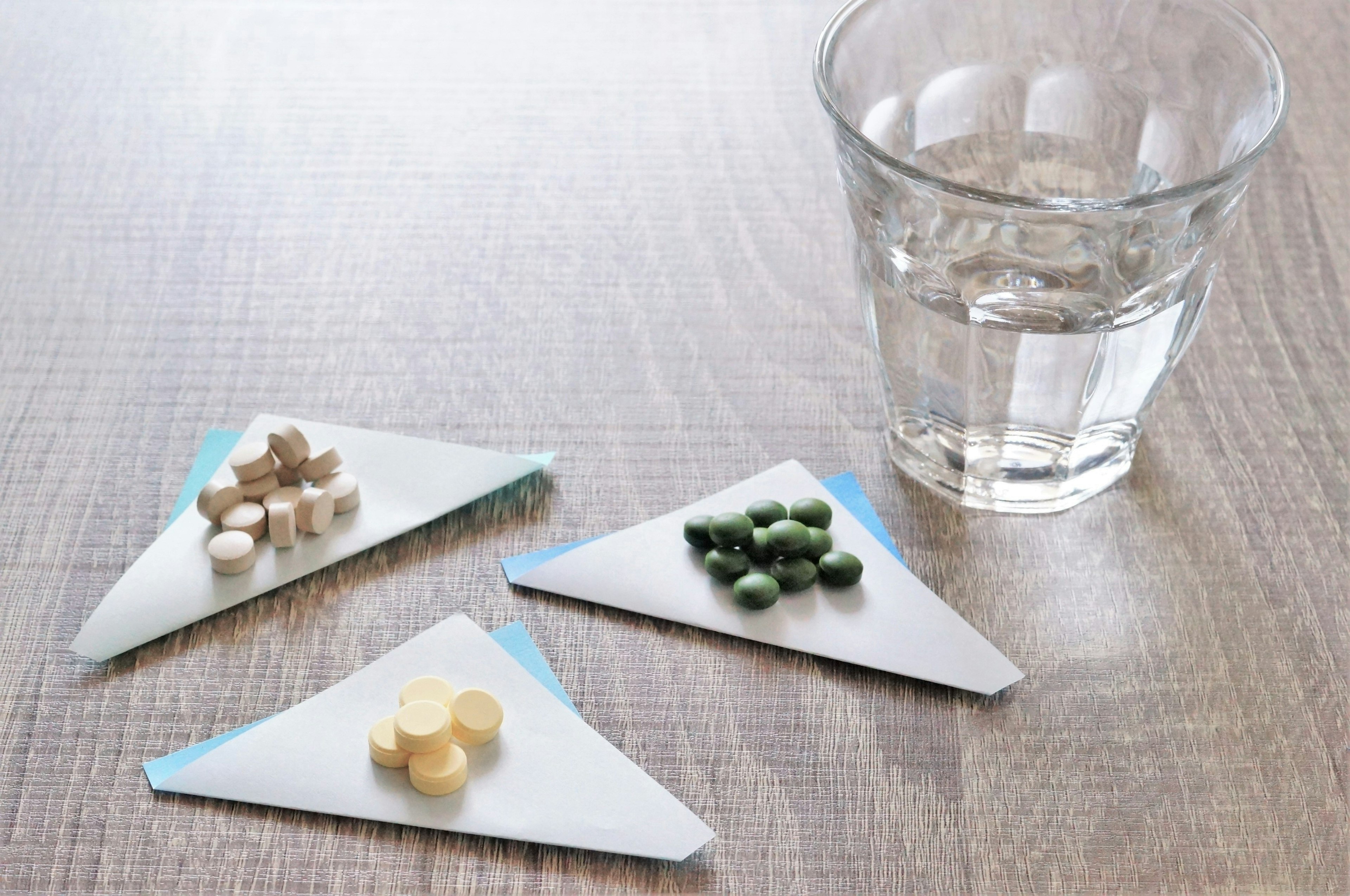 Different colored and shaped pills arranged on triangular plates next to a glass of water