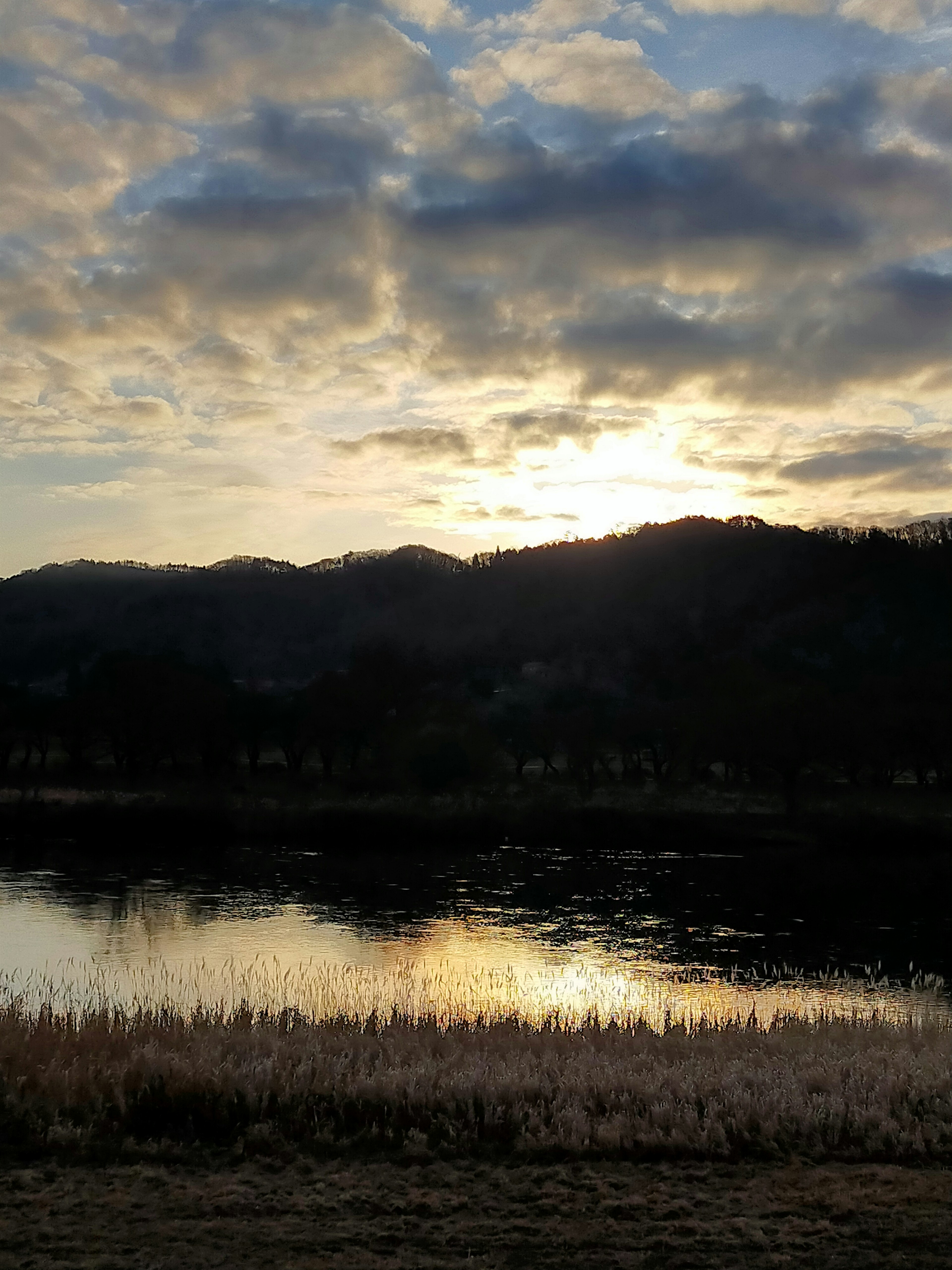 Scenic view of sunset behind mountains with reflections on water and grassy foreground