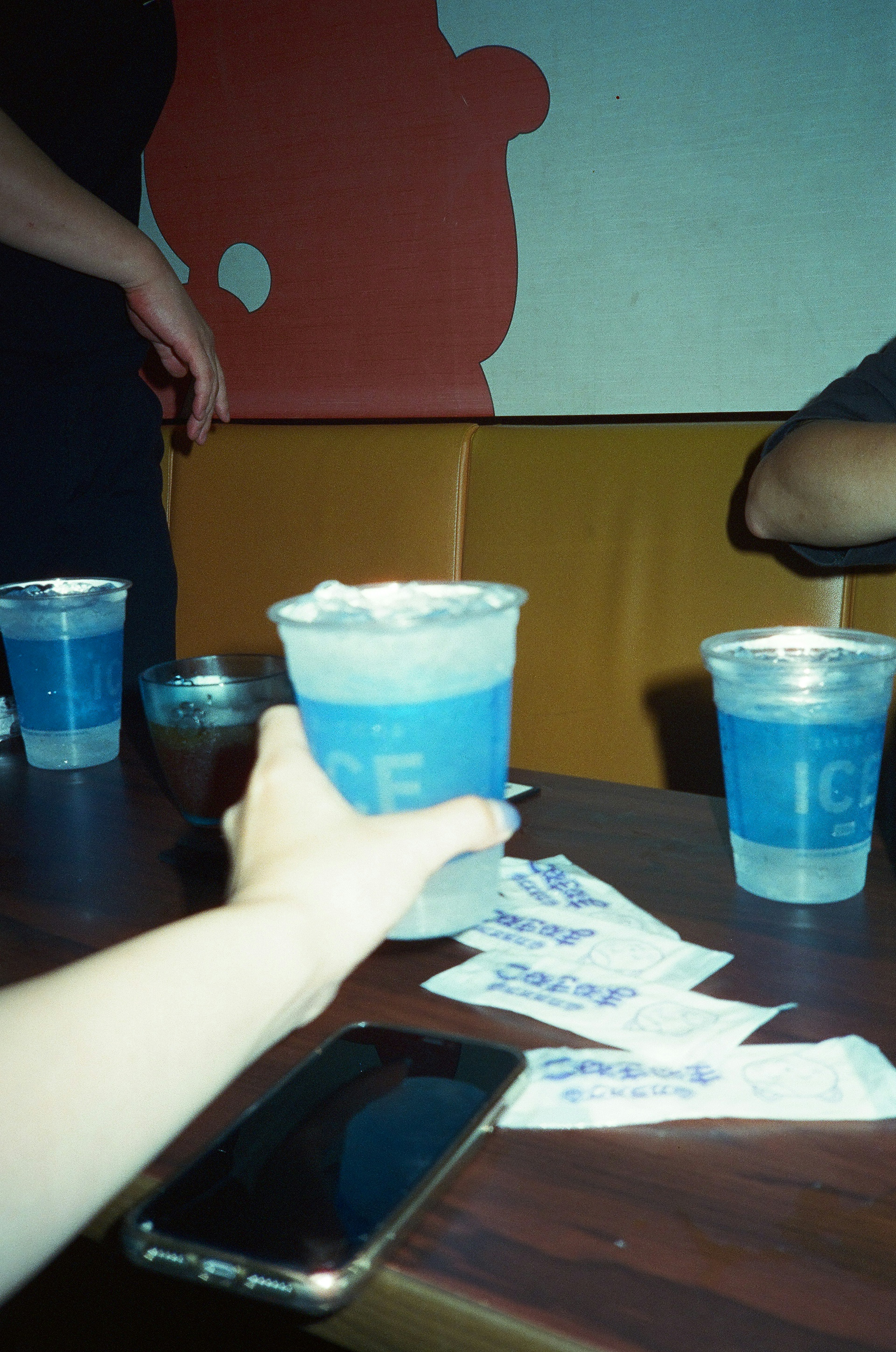 Hand holding a blue drink with other drinks on the table