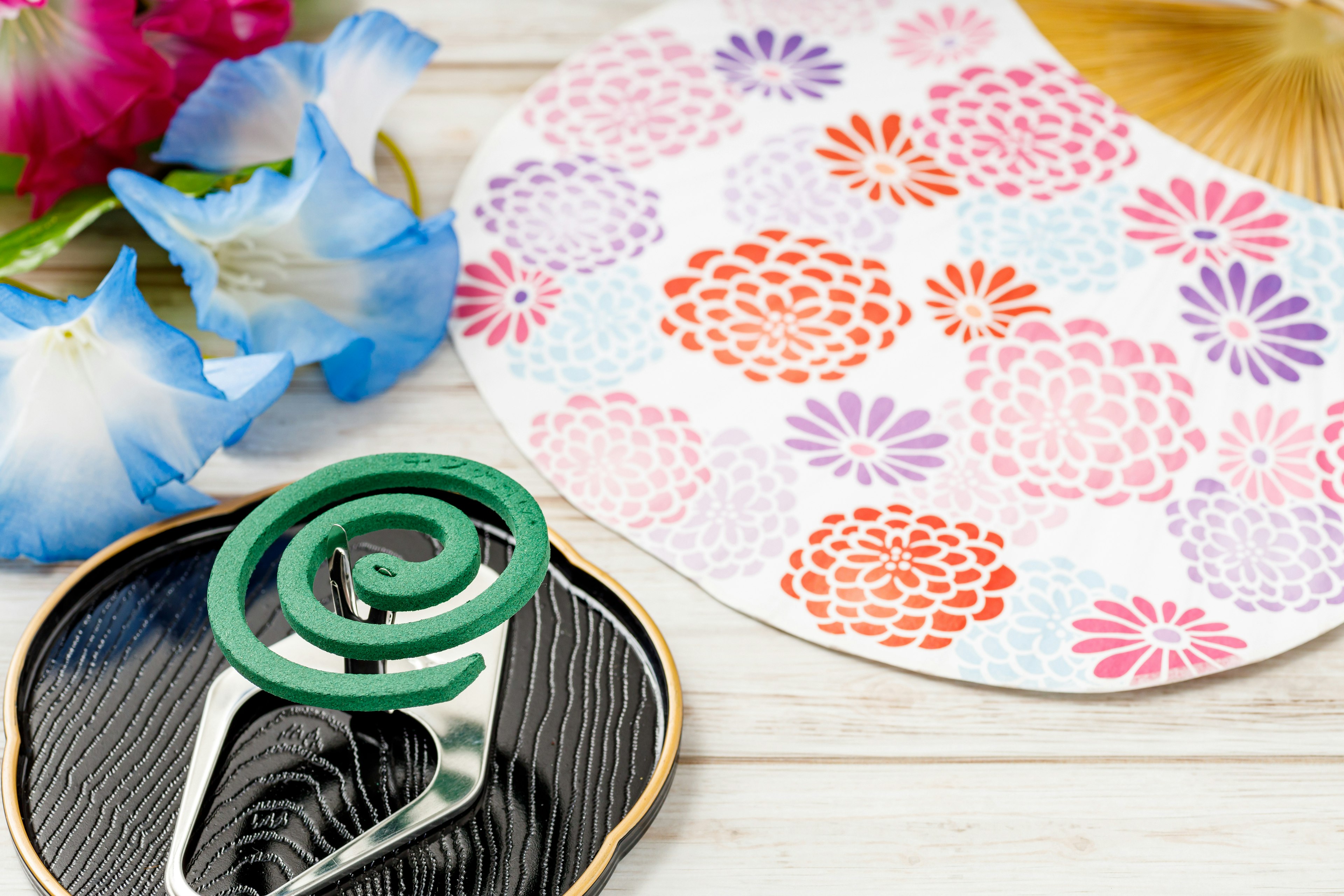 A decorative fan with floral patterns and a green spiral accessory on a wooden surface