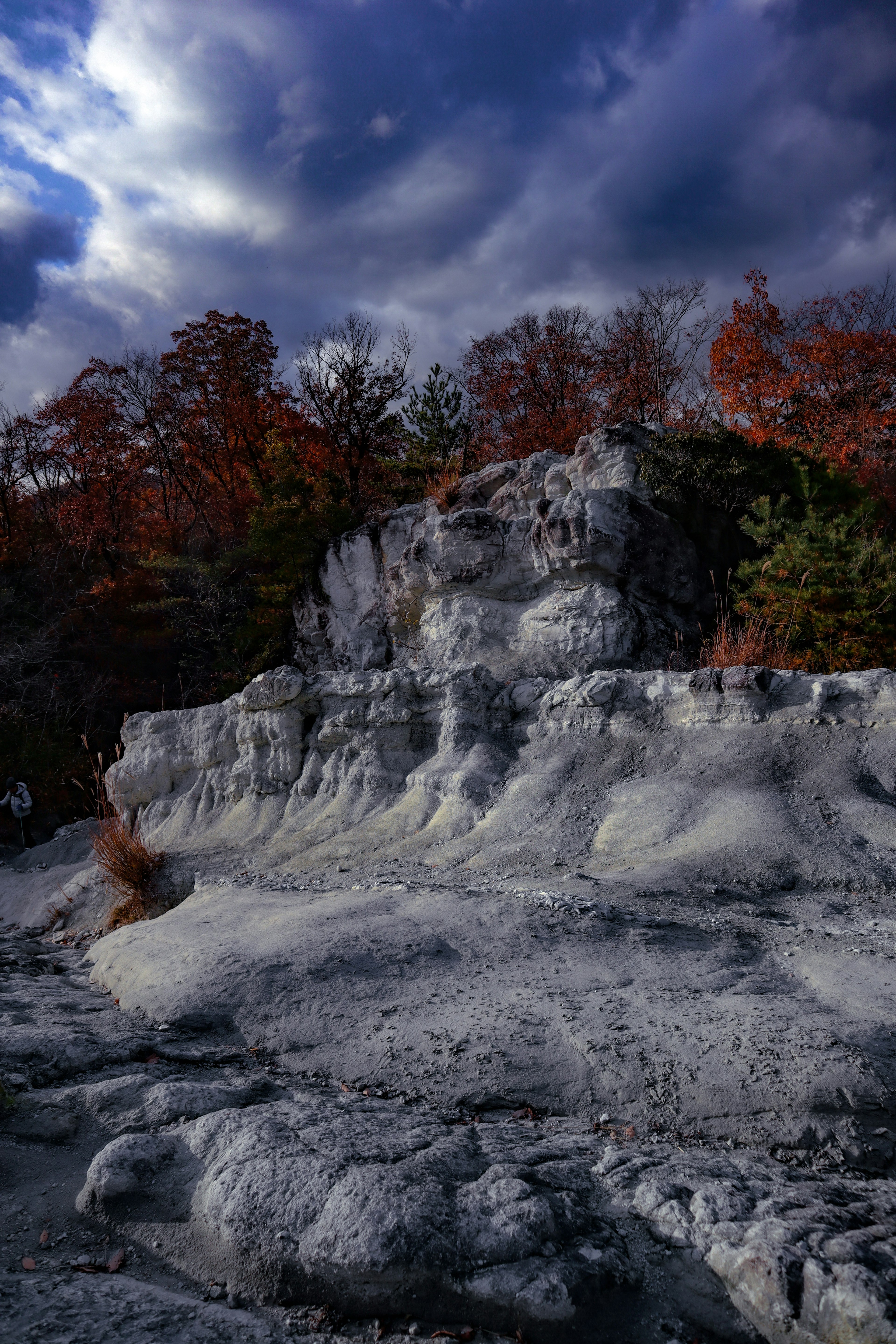 Felslandschaft umgeben von herbstlich gefärbten Bäumen und dynamischen Wolken