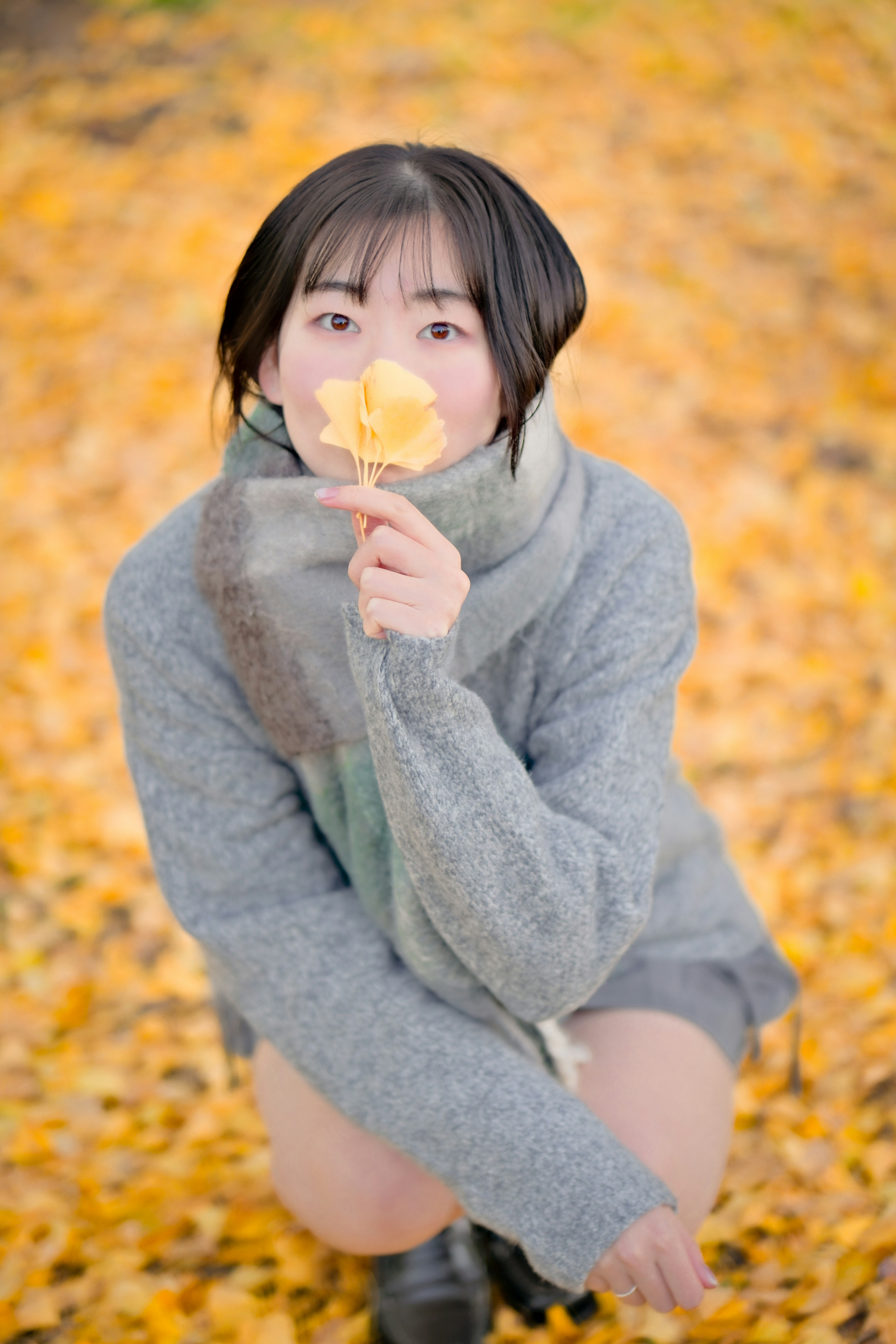 Mujer sosteniendo una flor amarilla entre hojas de otoño