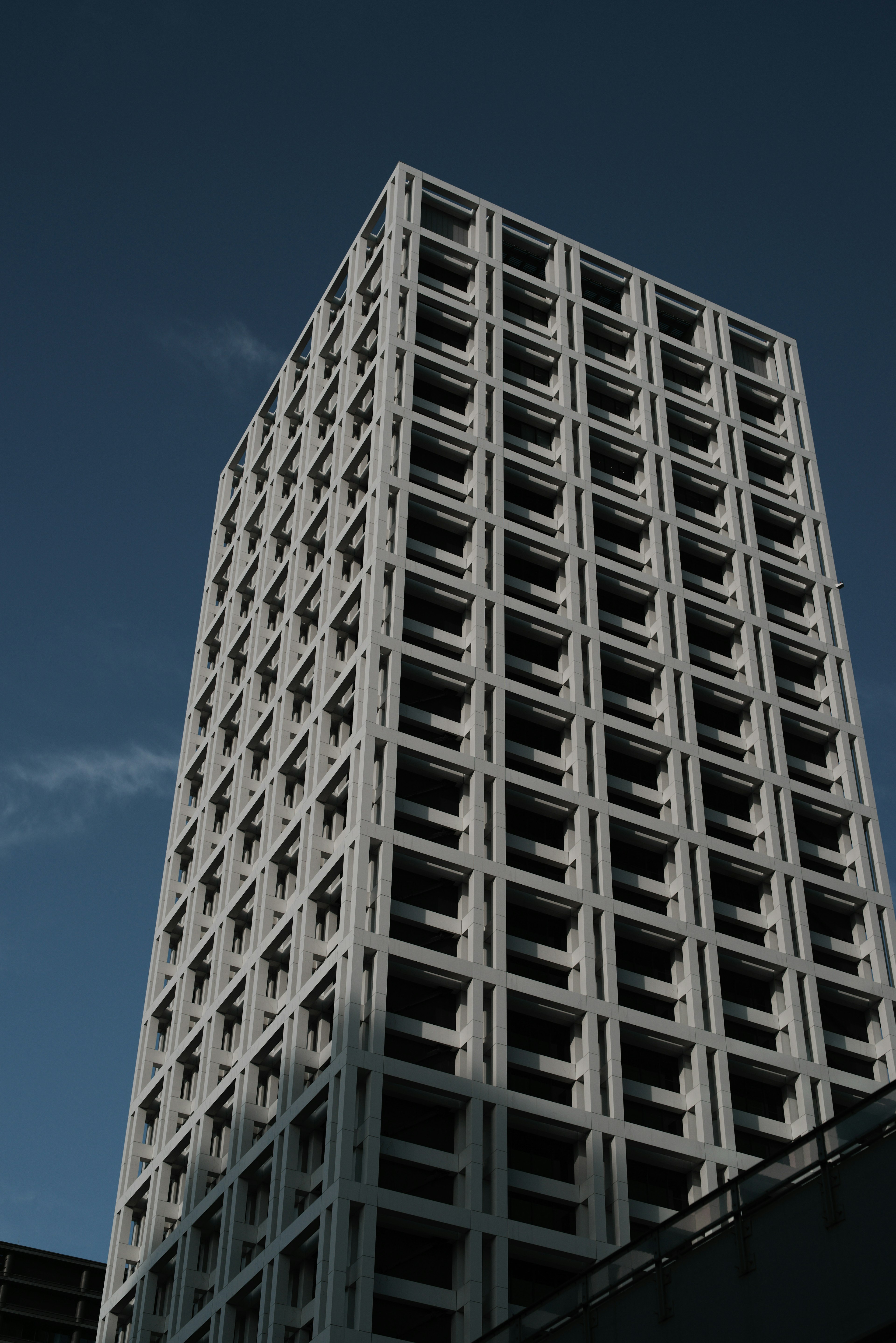 Extérieur d'un gratte-ciel avec une structure en béton blanc sur fond de ciel bleu présentant un agencement de fenêtres géométriques