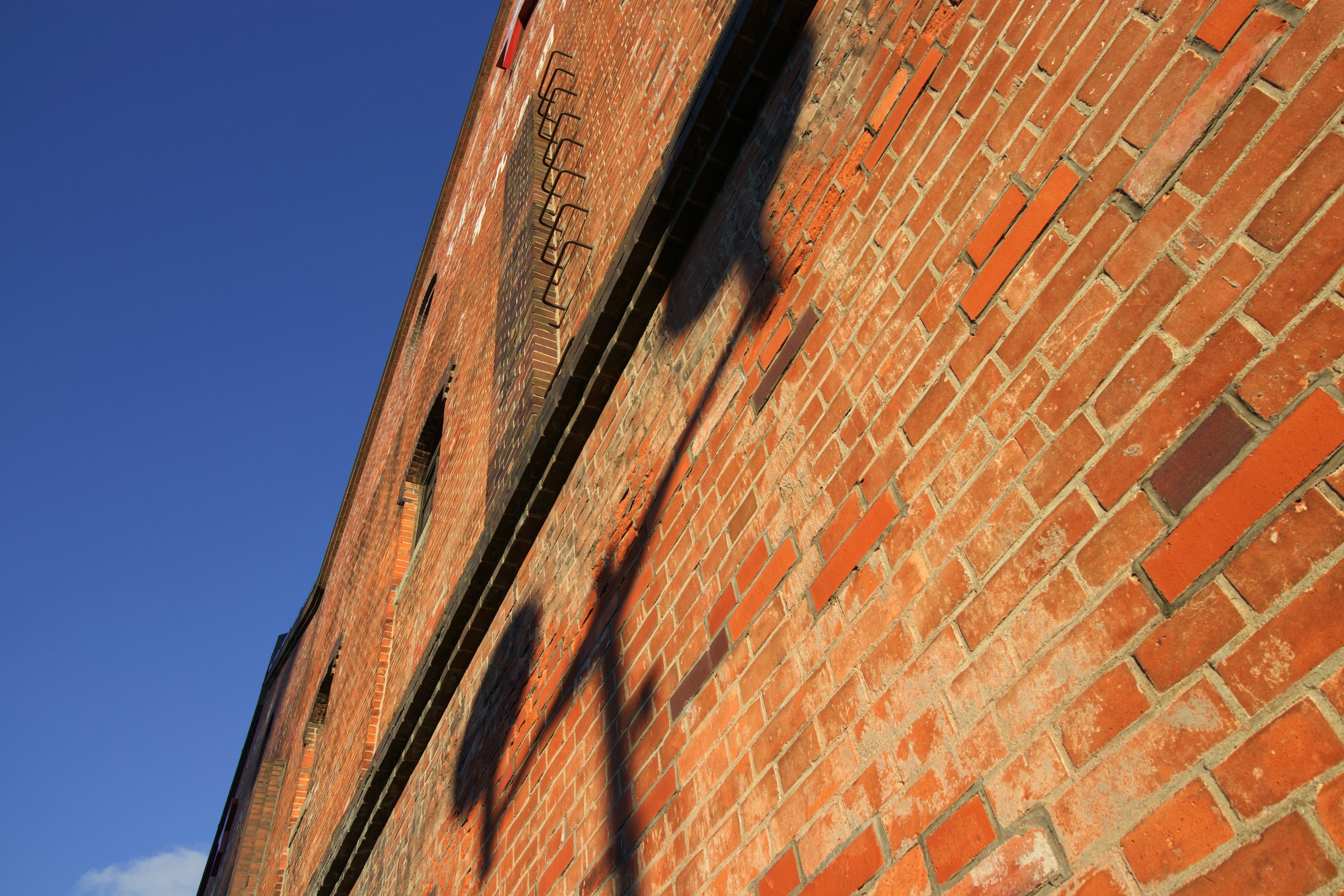 Pared de ladrillos rojos con sombras y cielo azul