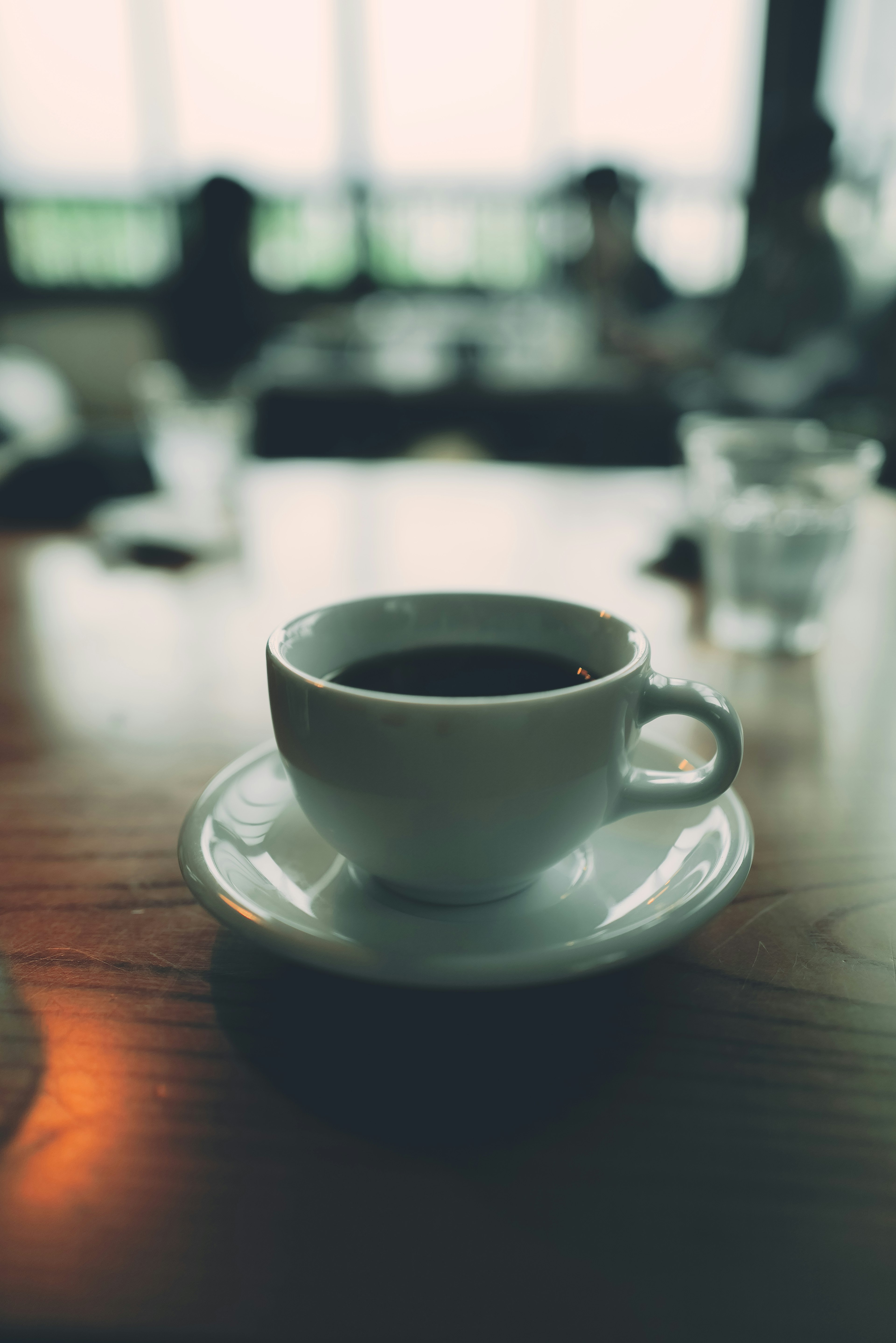 Coffee cup on a wooden table with a saucer blurred background with people