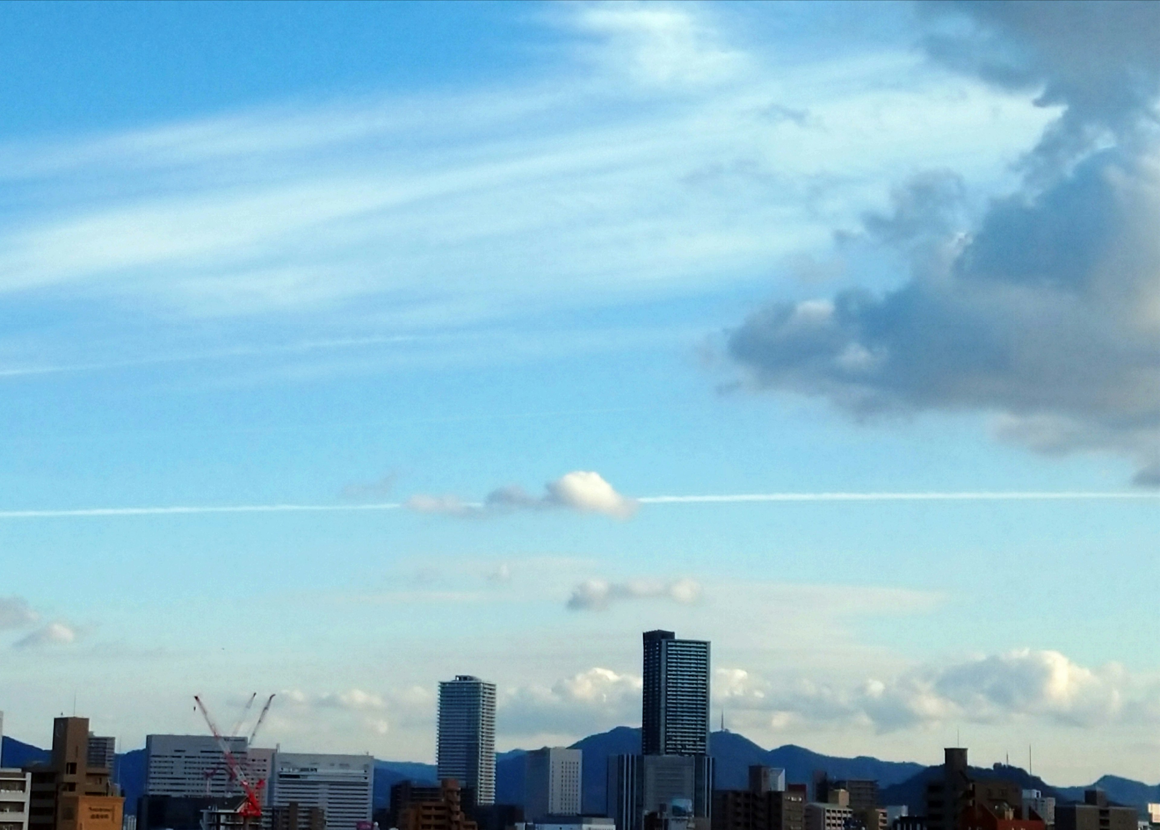 Stadtansicht mit blauem Himmel und Wolken sowie einem Kondensstreifen