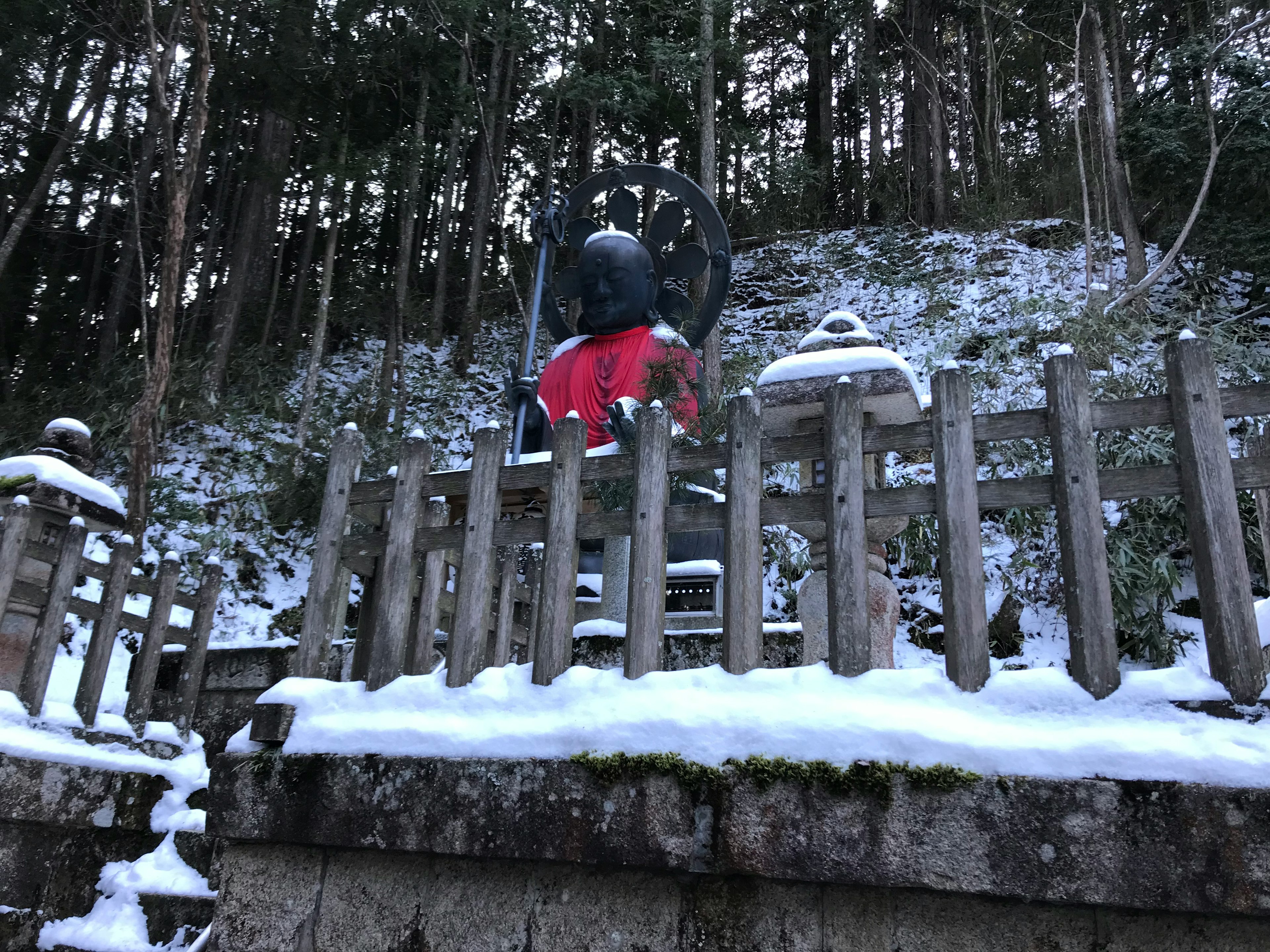 雪に覆われた山の中に立つ仏像と木製の柵を背景にした静かな風景