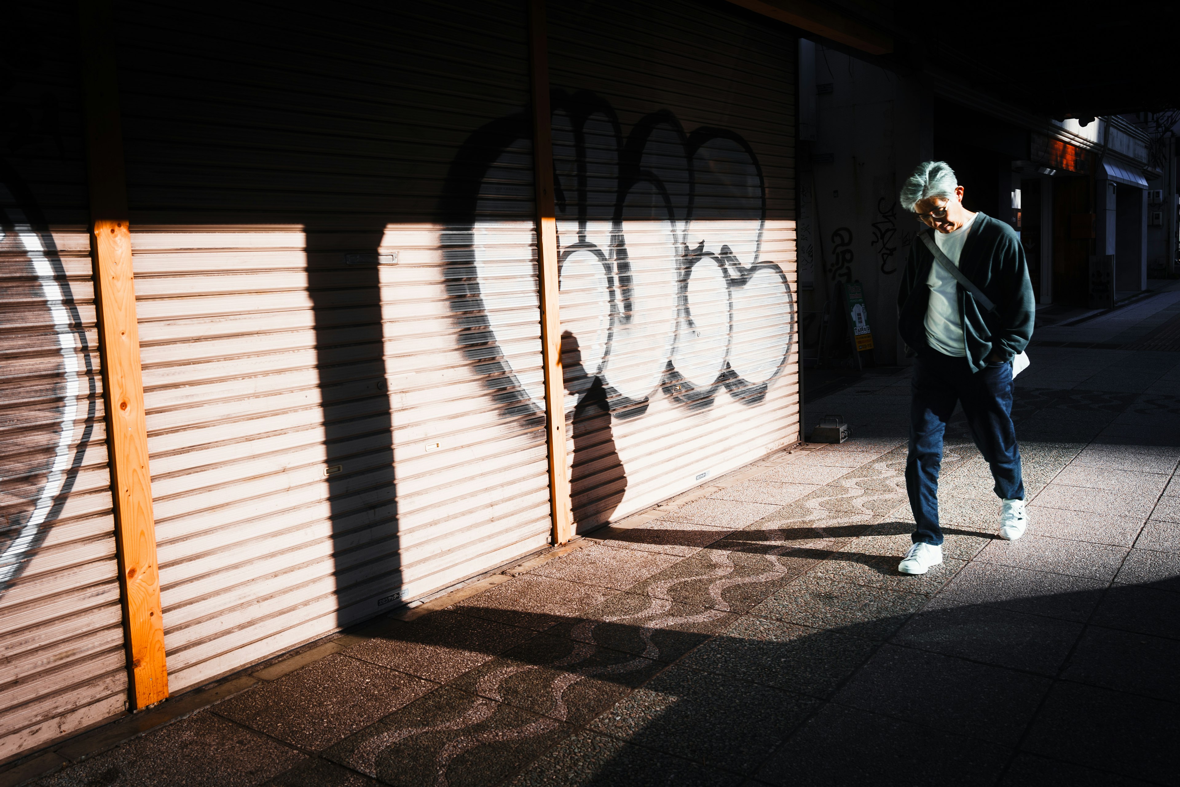 Man walking in front of a graffiti-covered shutter with shadows