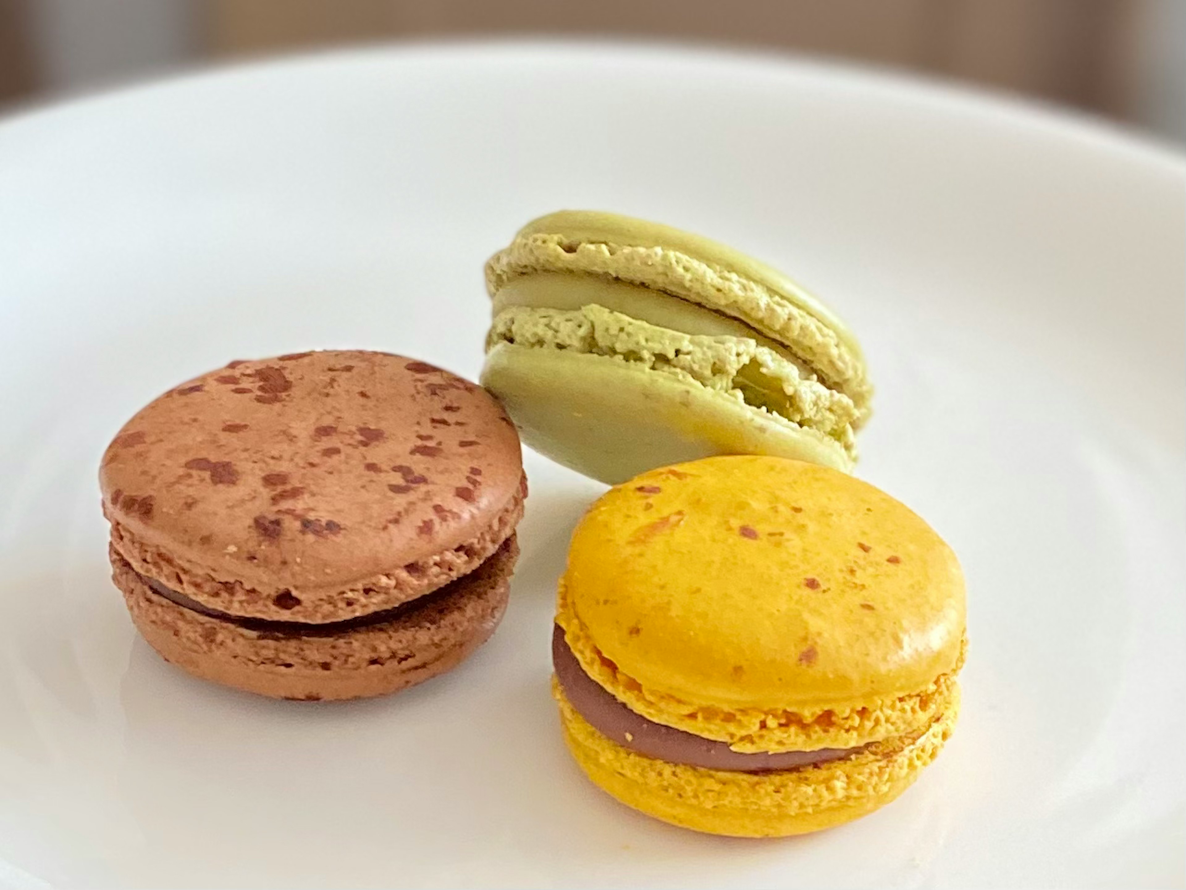 Trois macarons sur une assiette blanche avec des couleurs marron, jaune et verte