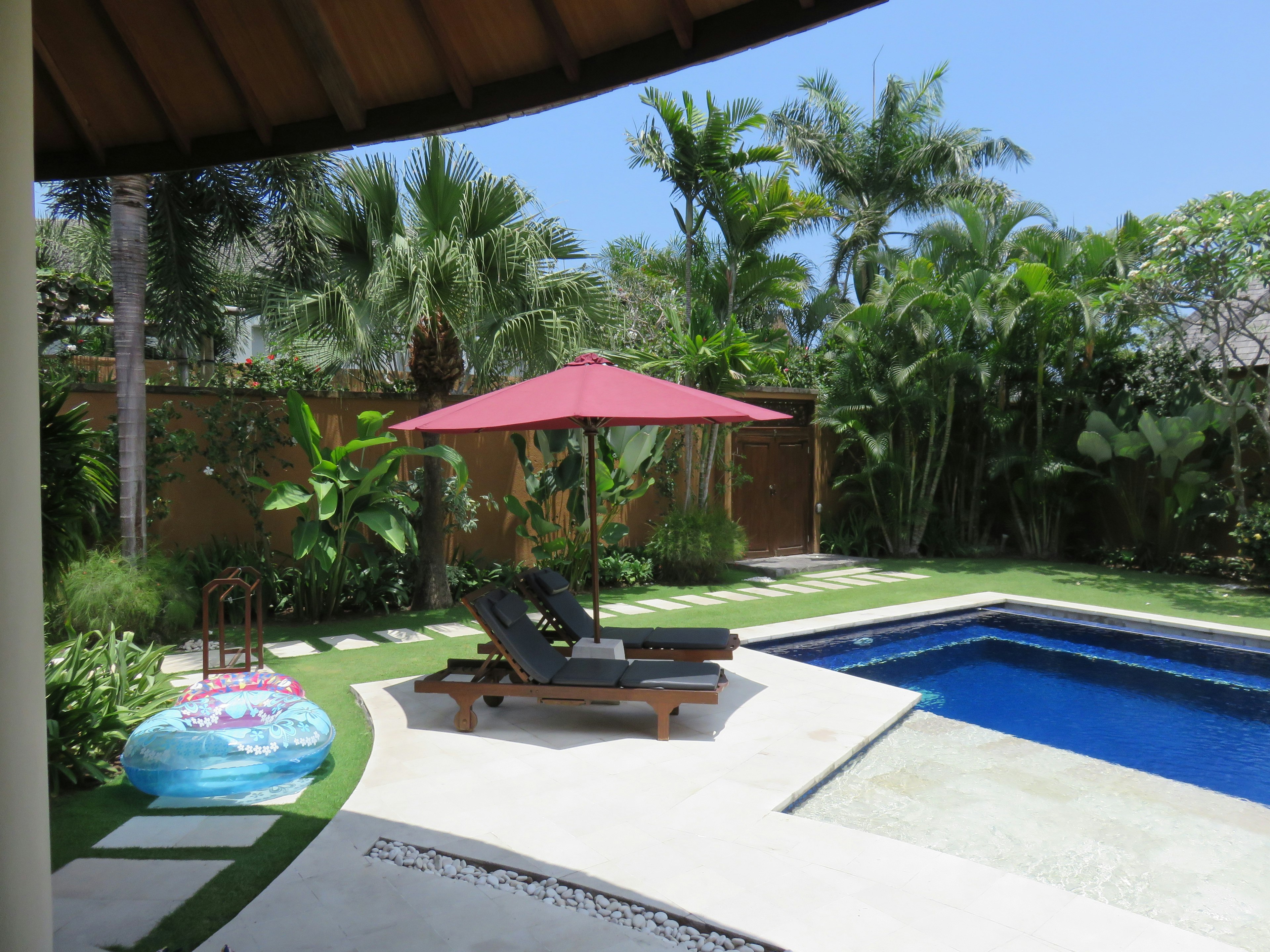 Black lounge chair with red umbrella by the pool surrounded by lush green plants