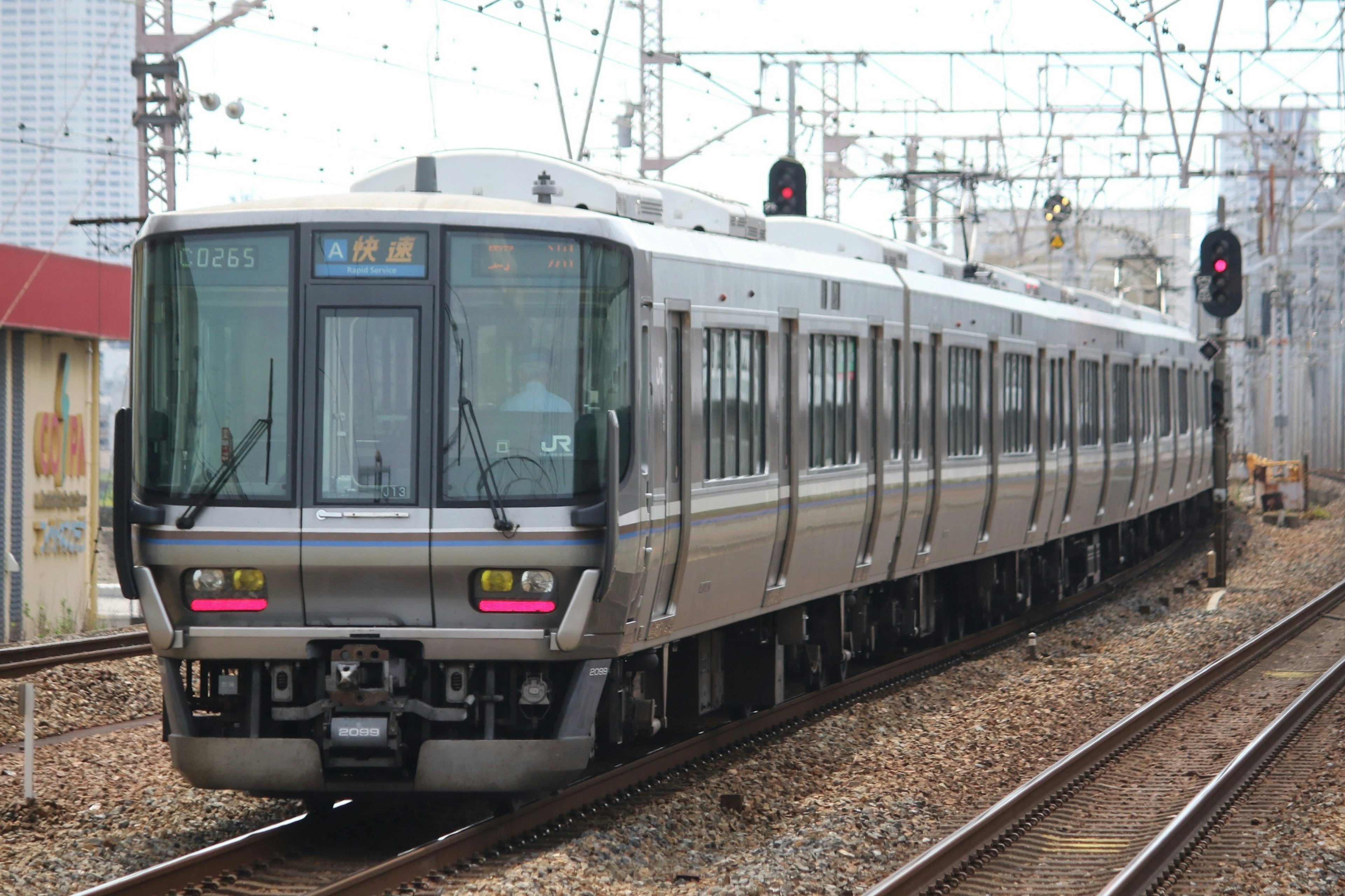 A silver train is running on the tracks with a red signal indicating stop