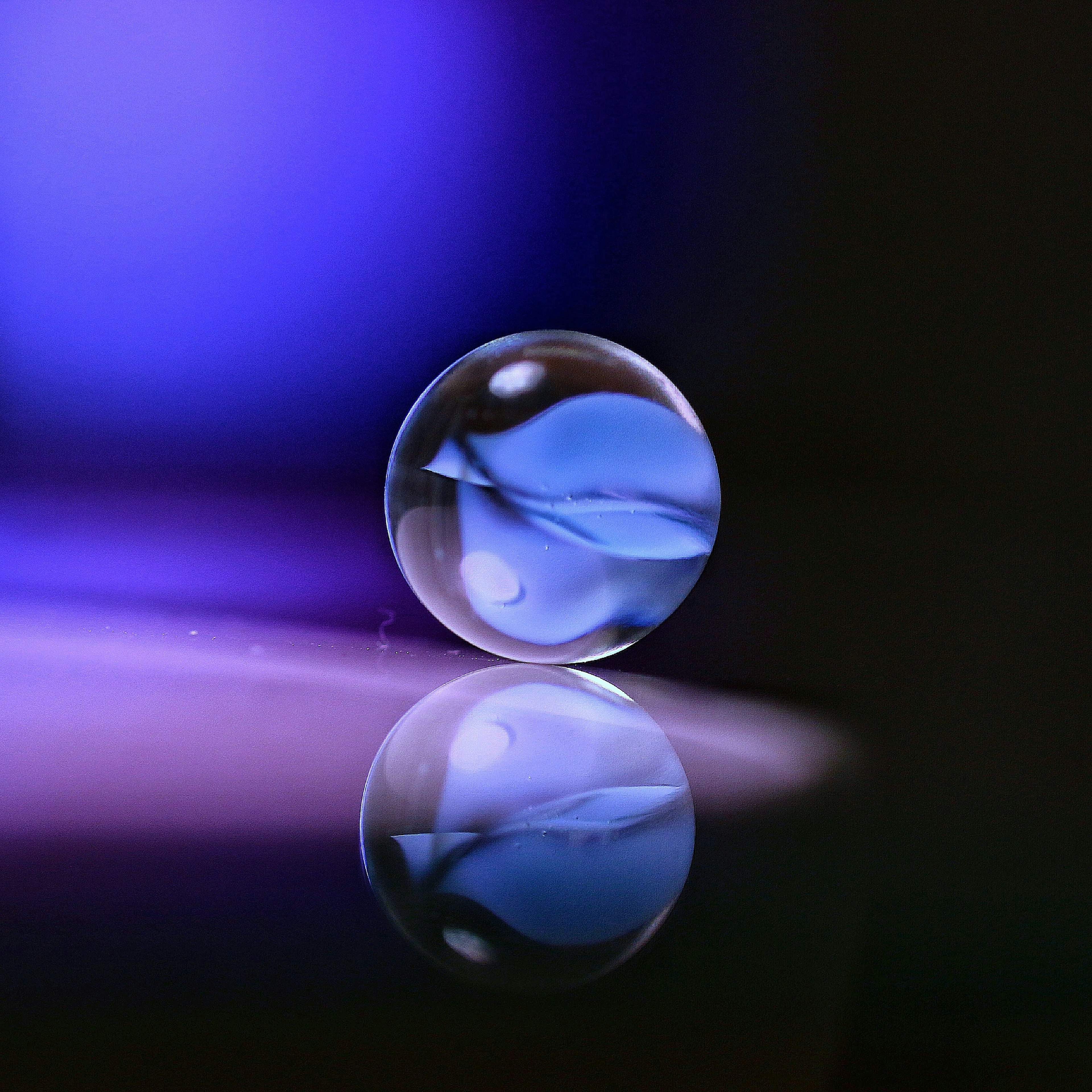 Una canica transparente con un patrón de hoja azul reflejándose en un fondo morado