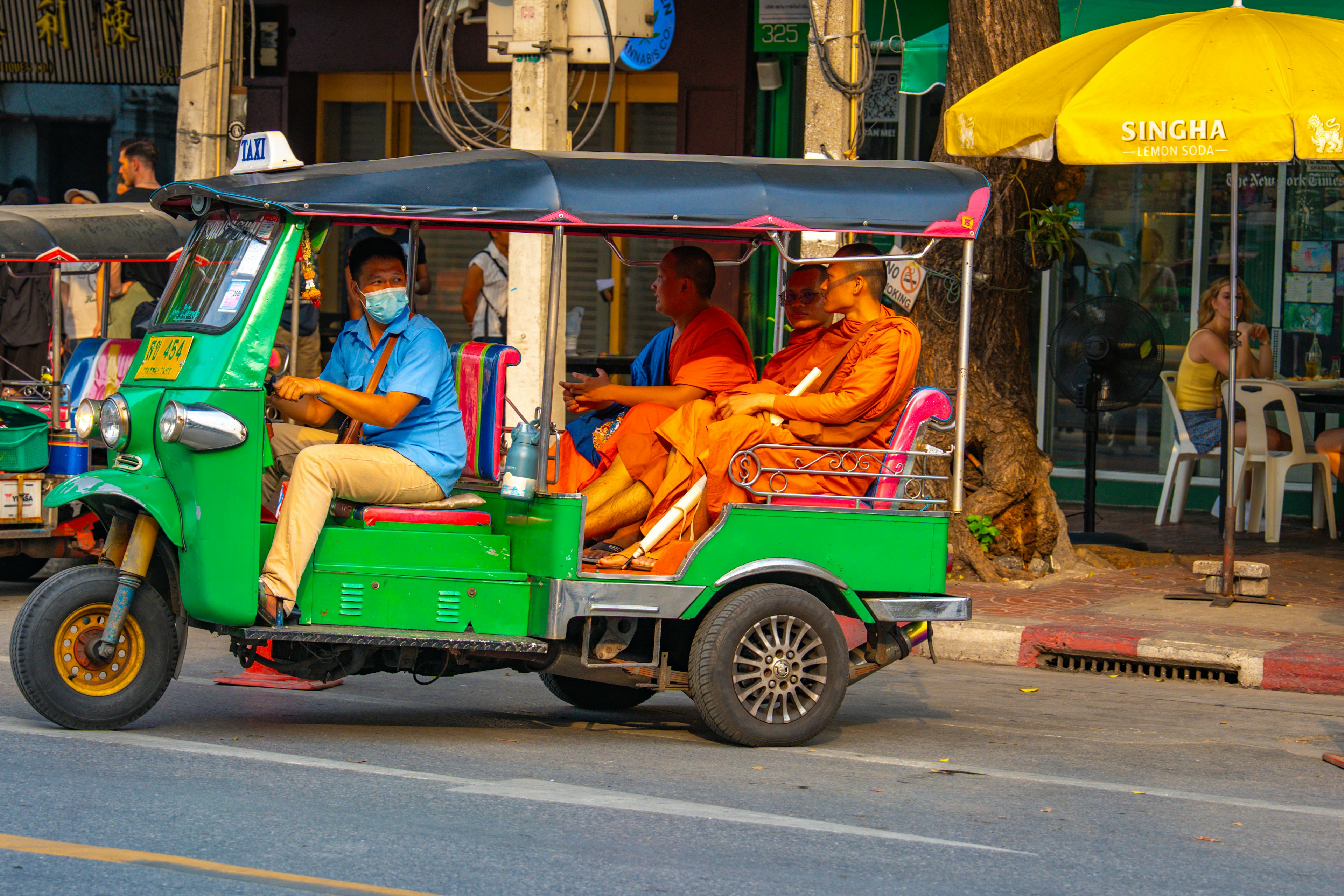 A green tuk-tuk with monks and a driver