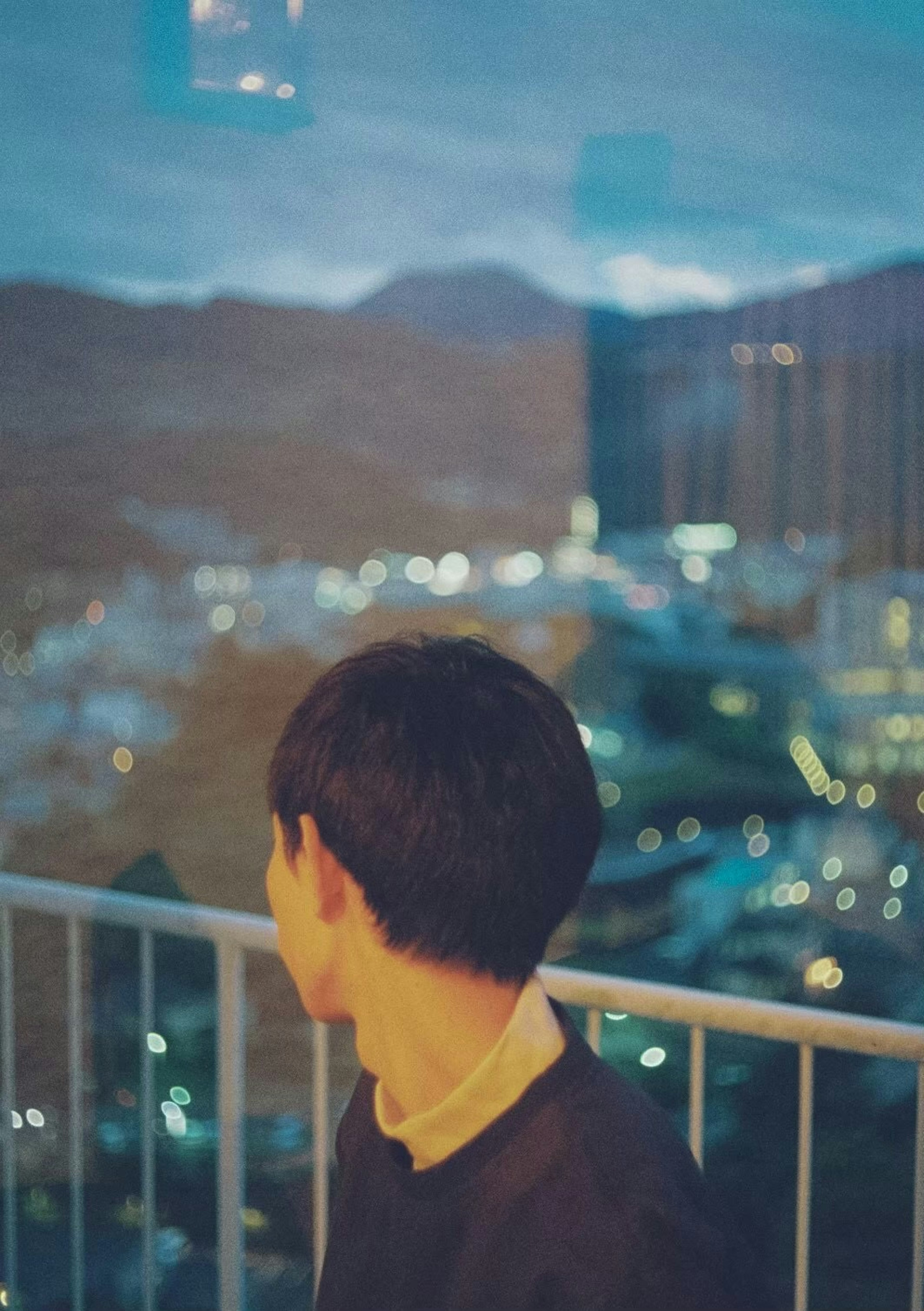 Young person gazing out the window with city lights in the background