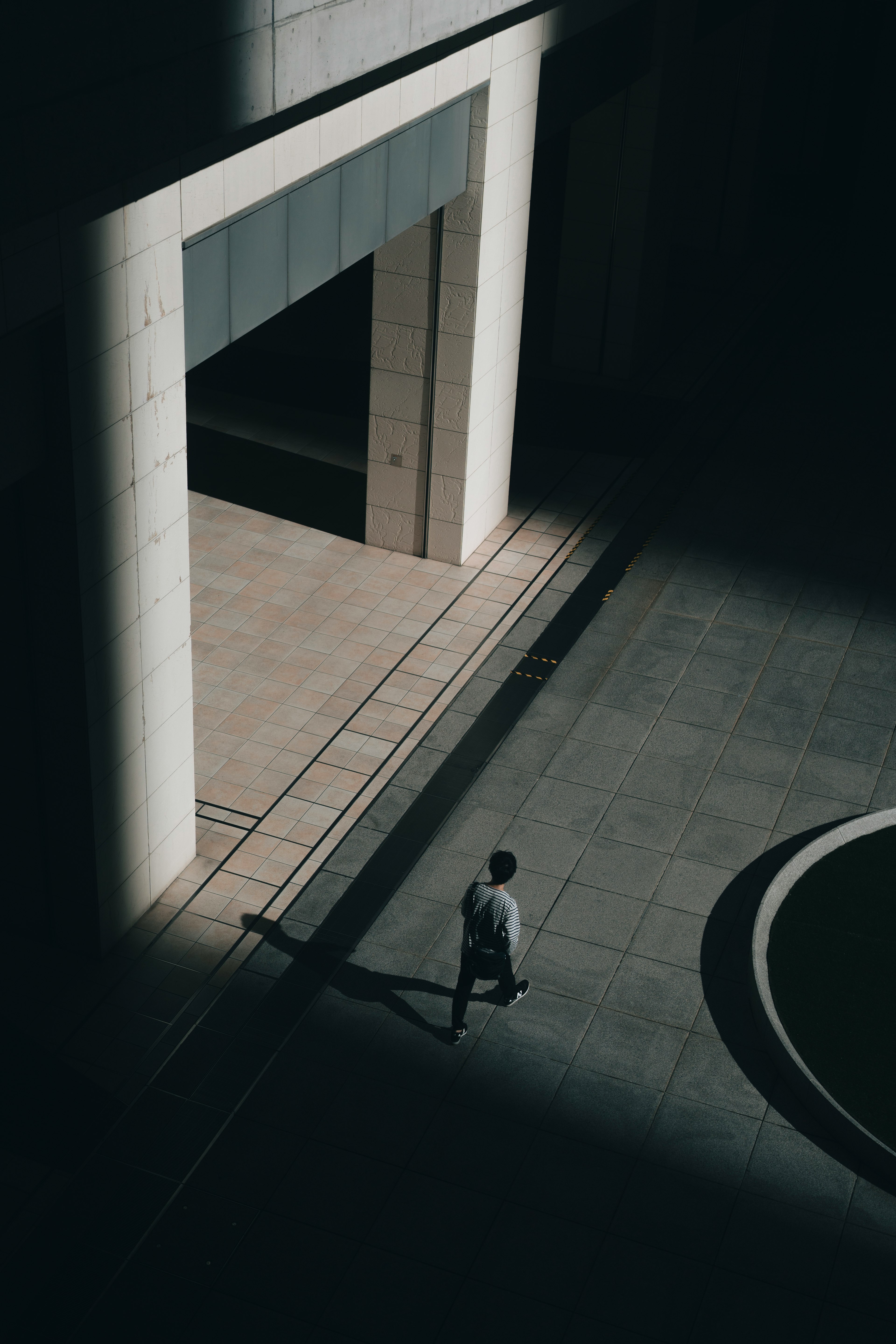 Person walking in a dimly lit area with a large white entrance of a building visible