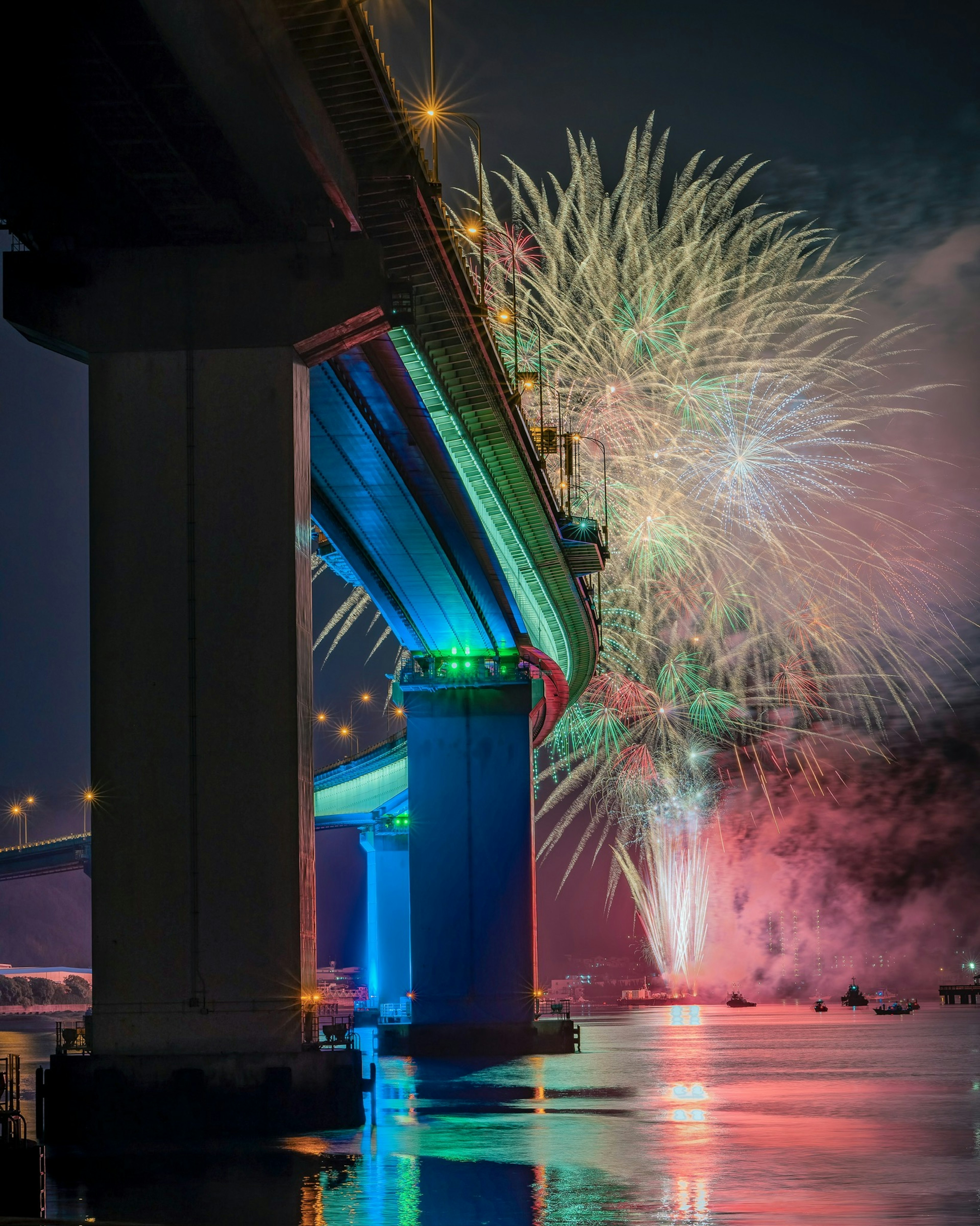 Feu d'artifice sous un pont la nuit reflets colorés sur l'eau