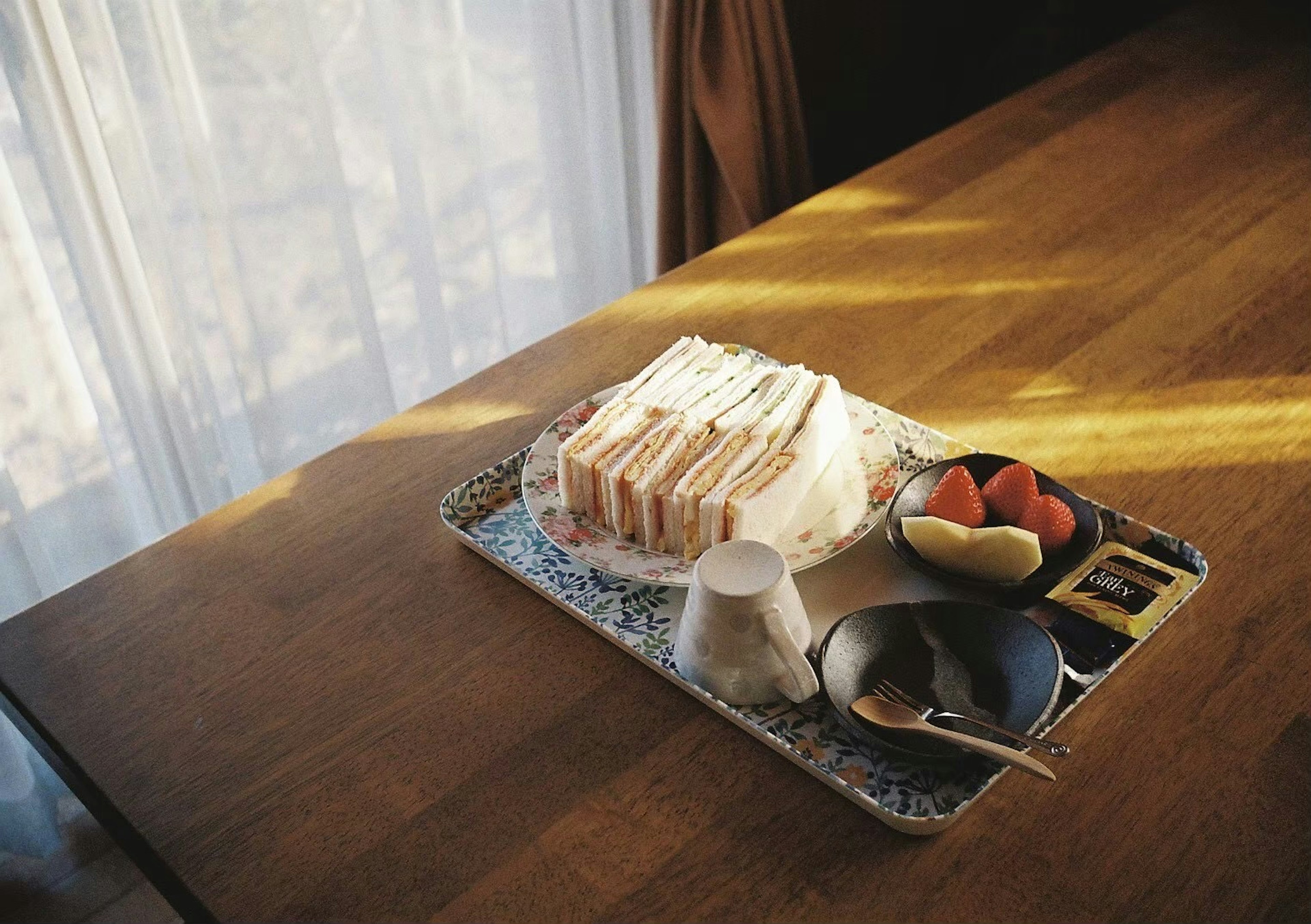 A tray with sandwiches and a fruit platter on a wooden table