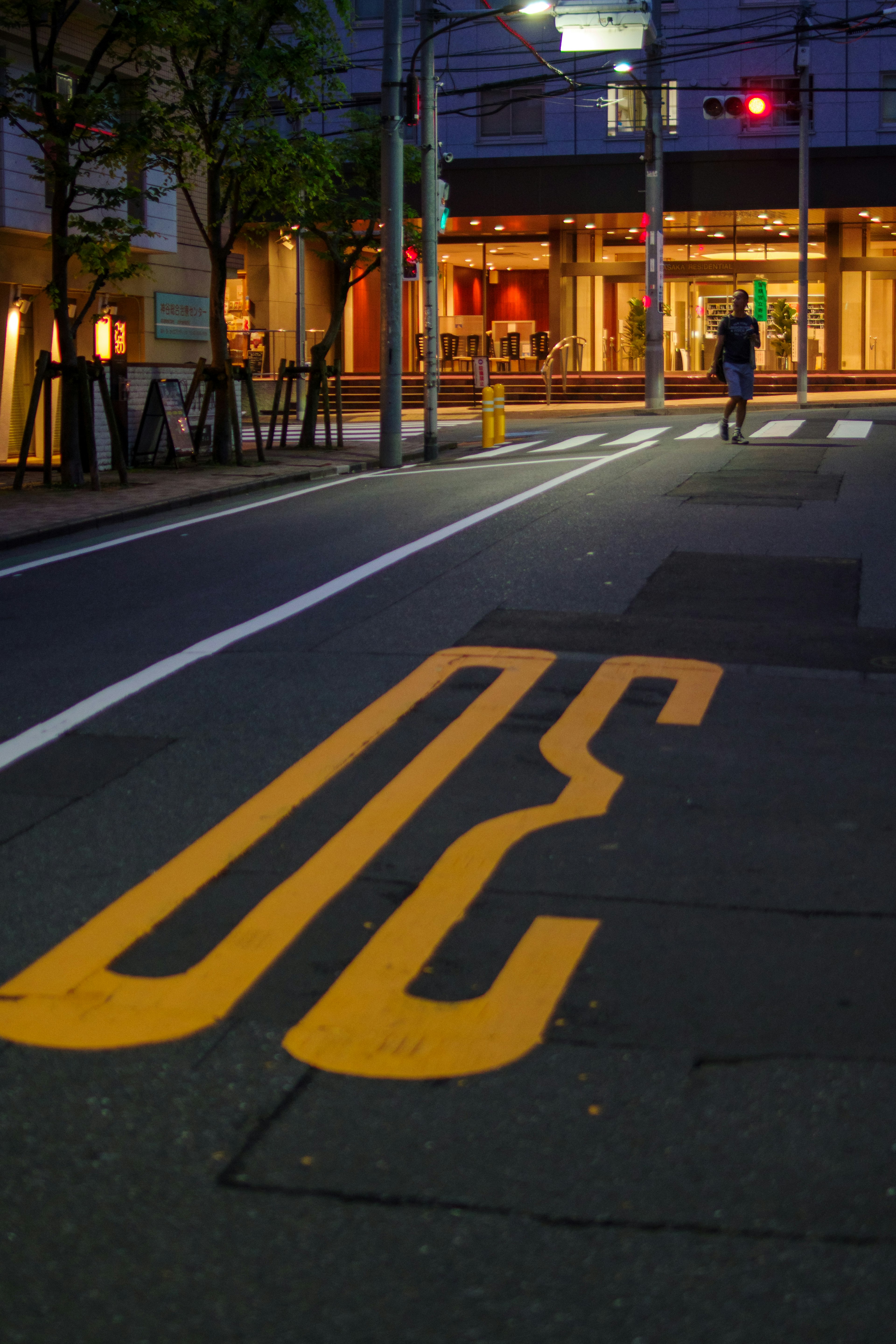 Yellow road marking on a street with a brightly lit building in the background at night