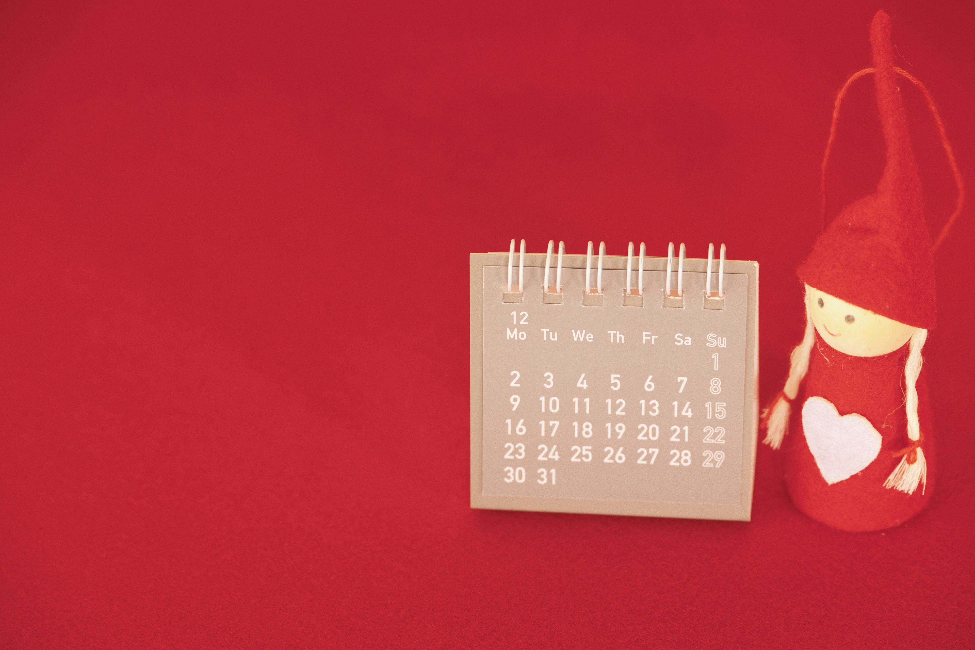 A calendar on a red background with a doll featuring a heart design