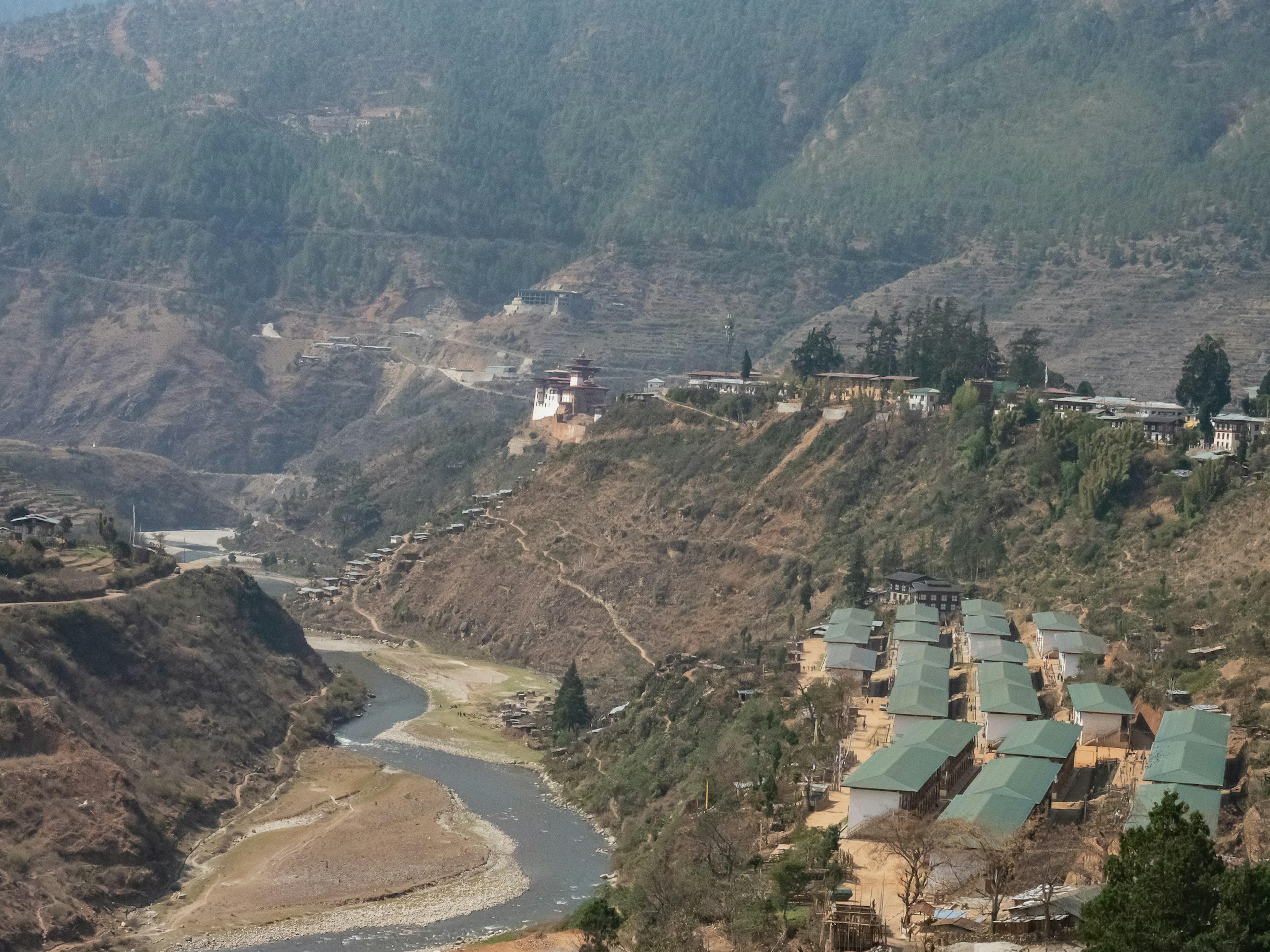 Vista escénica de un pequeño pueblo con casas de techo verde a lo largo de un río rodeado de montañas