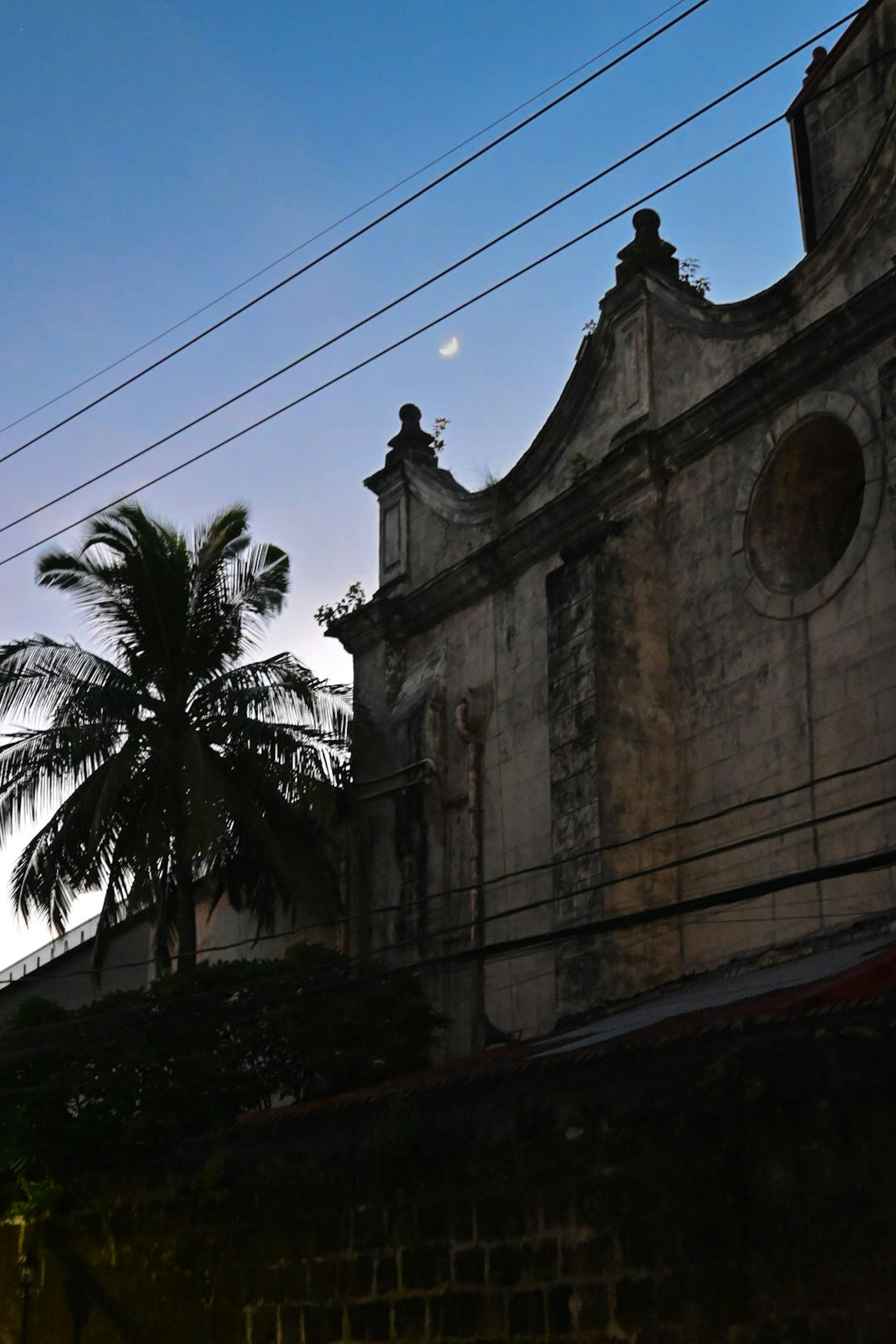 Mur d'un vieux bâtiment avec une lune visible dans le ciel du soir