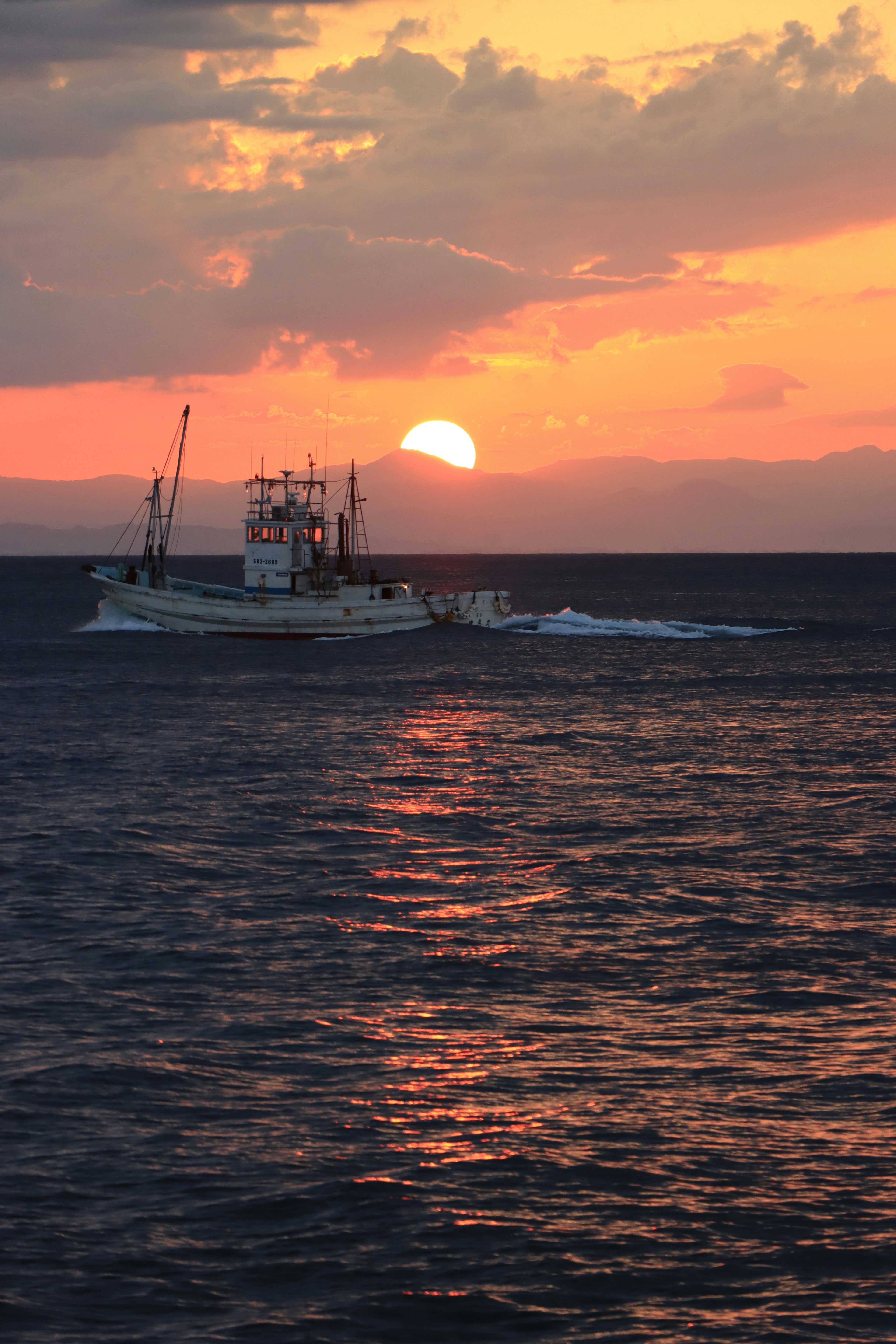 Silhouette eines Fischereibootes, das gegen den Sonnenuntergang segelt