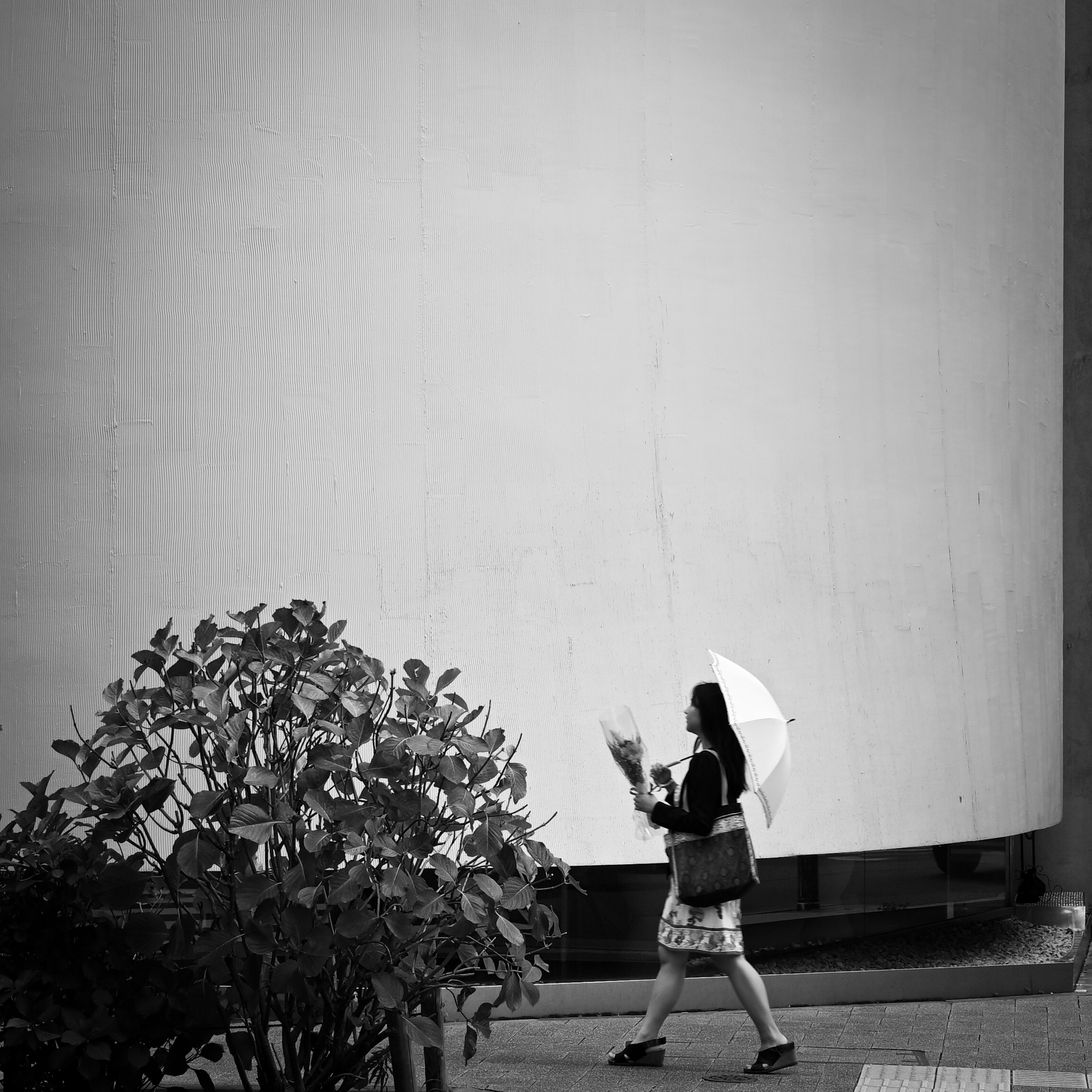 白い傘を持った女性が歩いているモノクロの街の風景