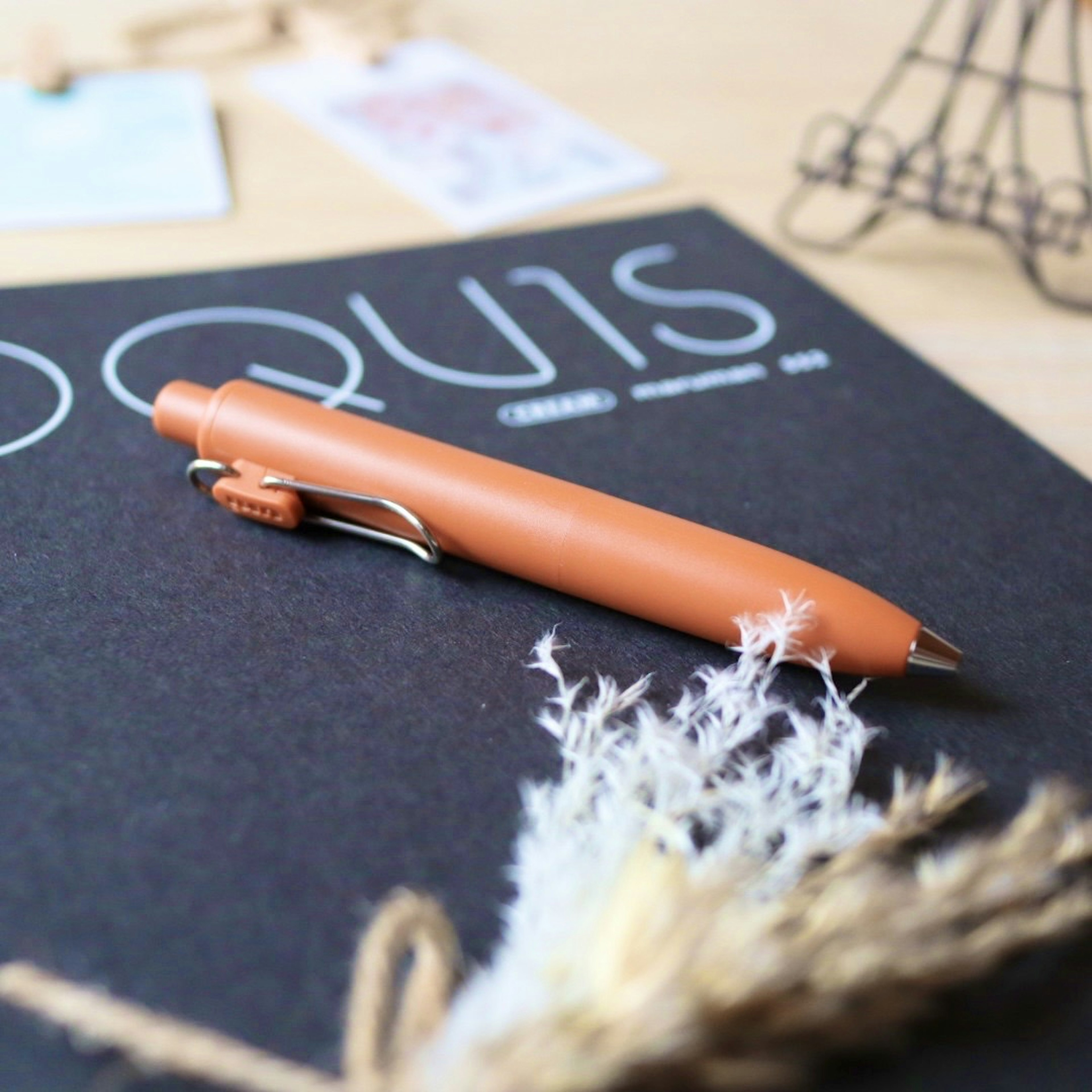 An orange pen resting on a black notebook with decorative elements