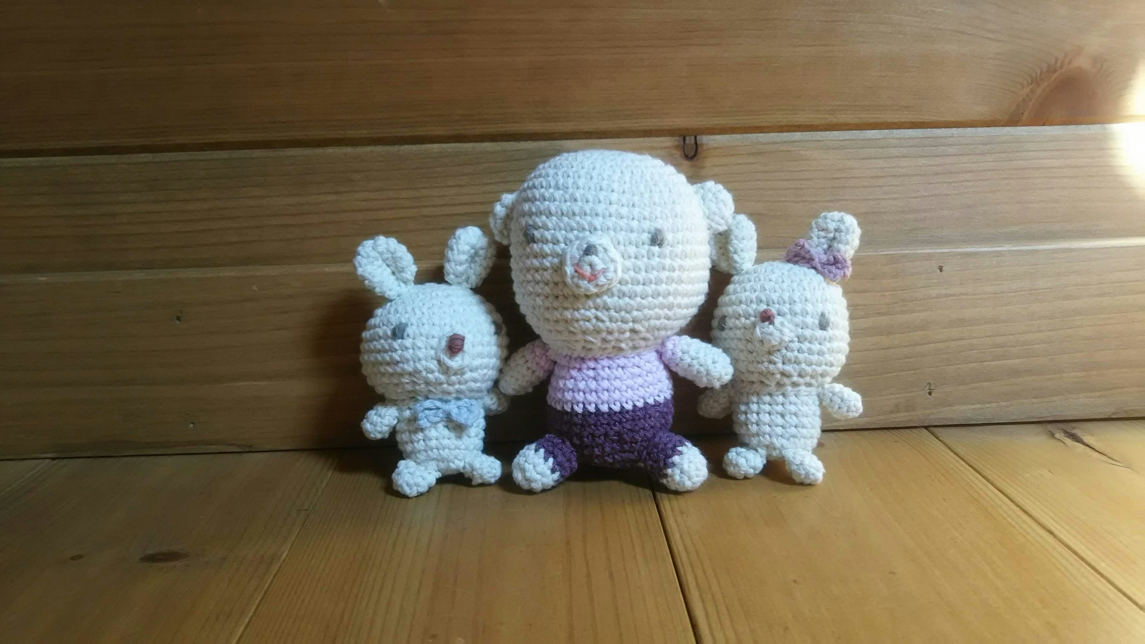 A collection of three crochet plush toys featuring a white rabbit a pig in pink clothing and a small rabbit